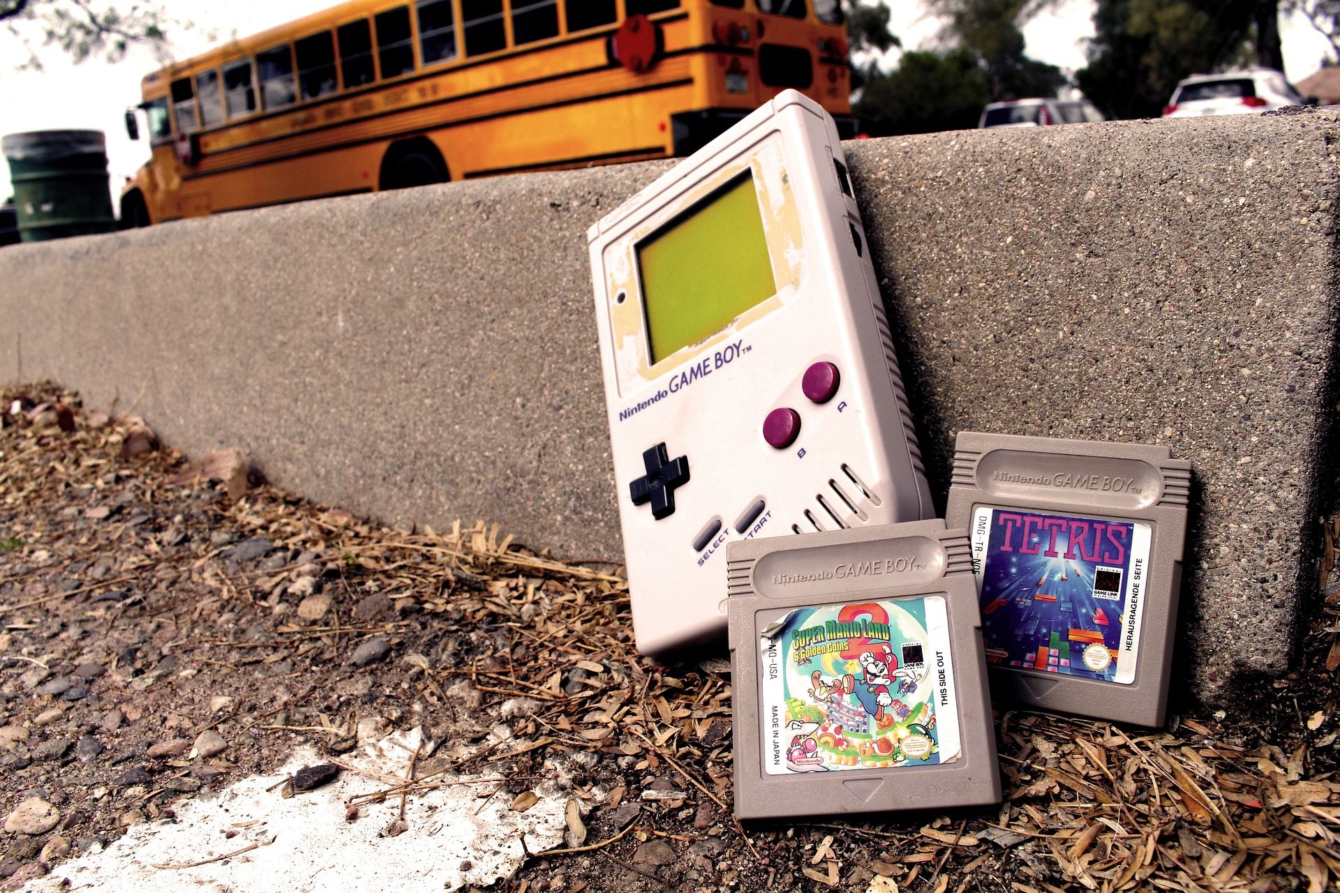 A Nintendo Gameboy resting against a concrete curb with a Tetris and a Mario Brothers game cartridge next to it.