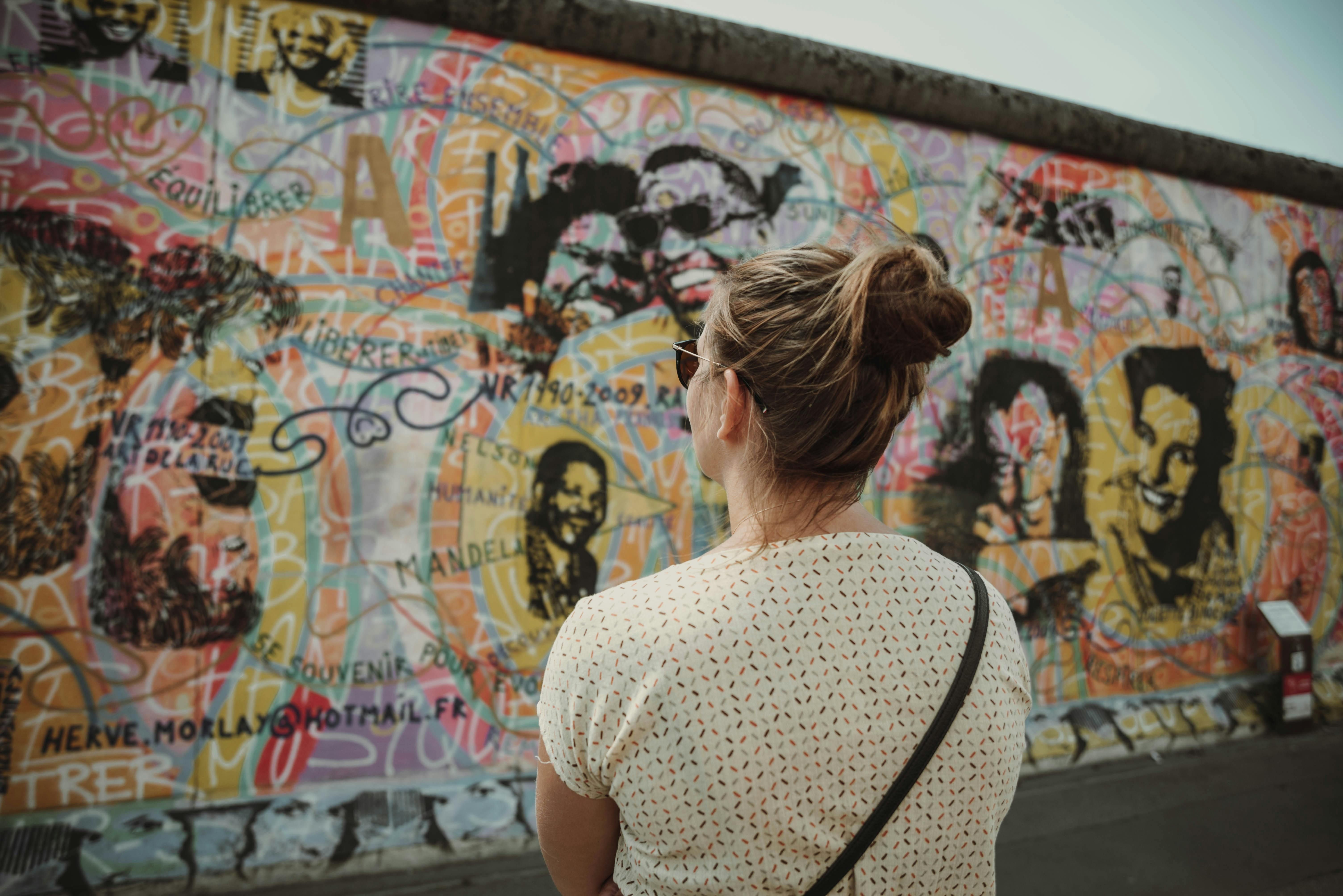 A woman stands in front of the Berlin Wall, which is covered in colorful grafitti.