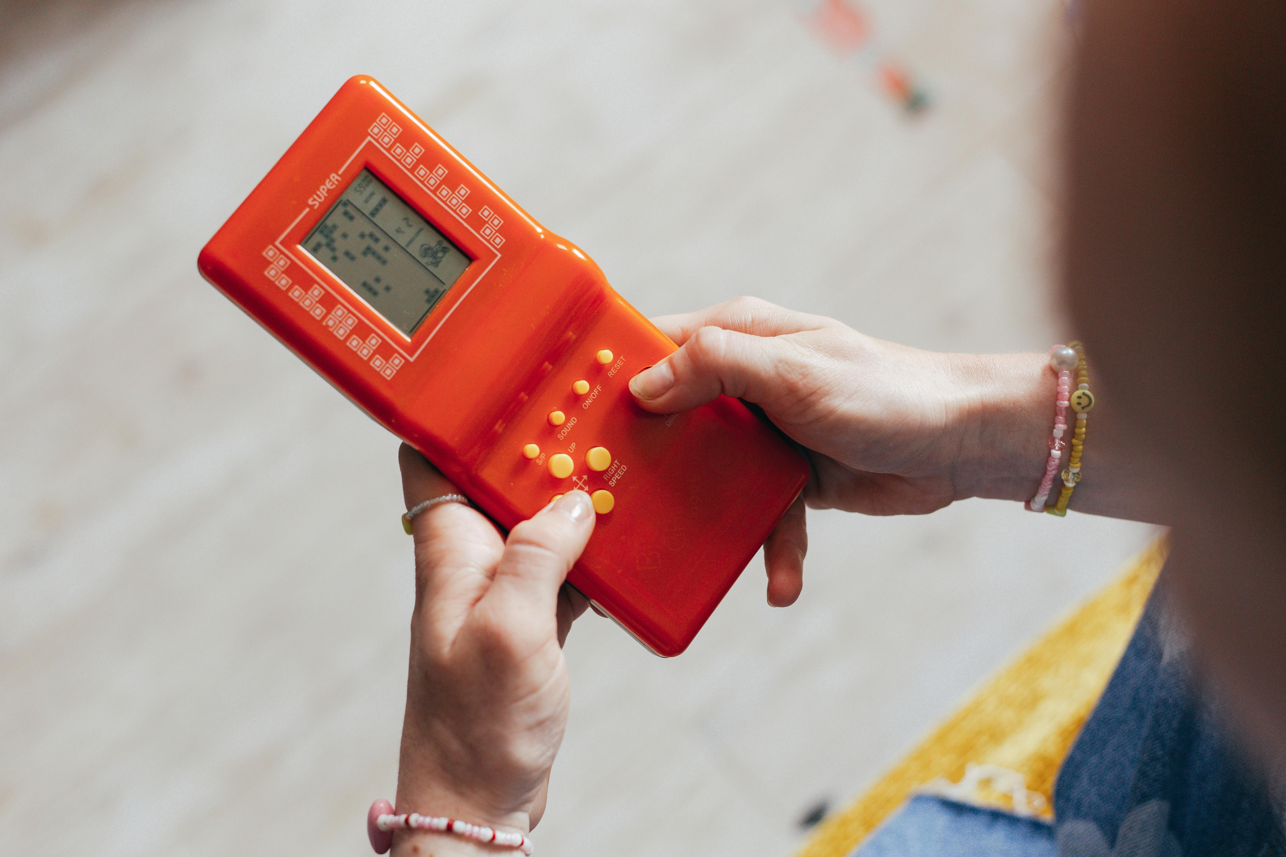 A woman holding an orange handheld console and playing a black-and-white version of Tetris.