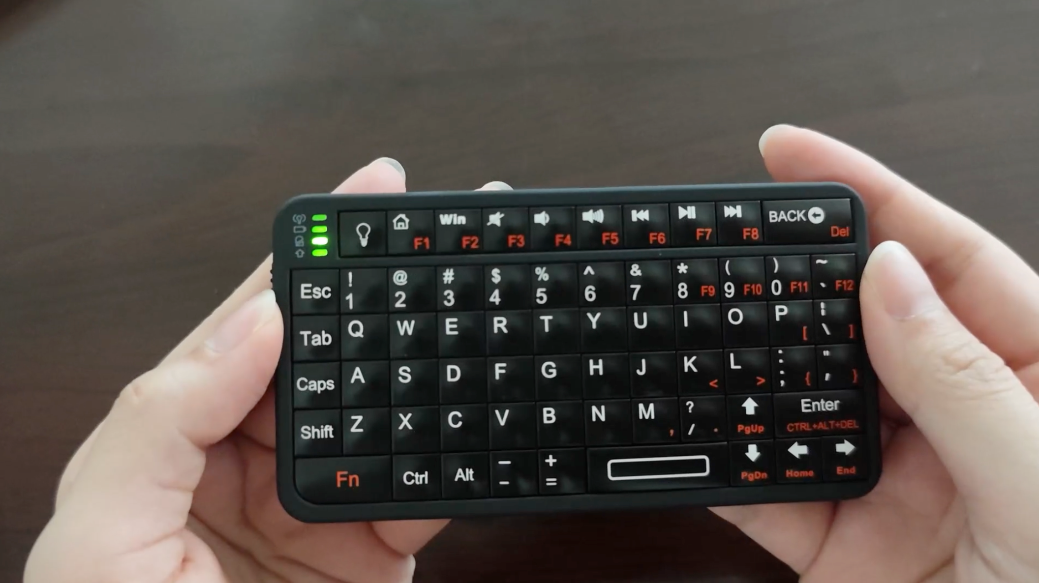 A mini bluetooth keyboard in hands in front of a wooden desk