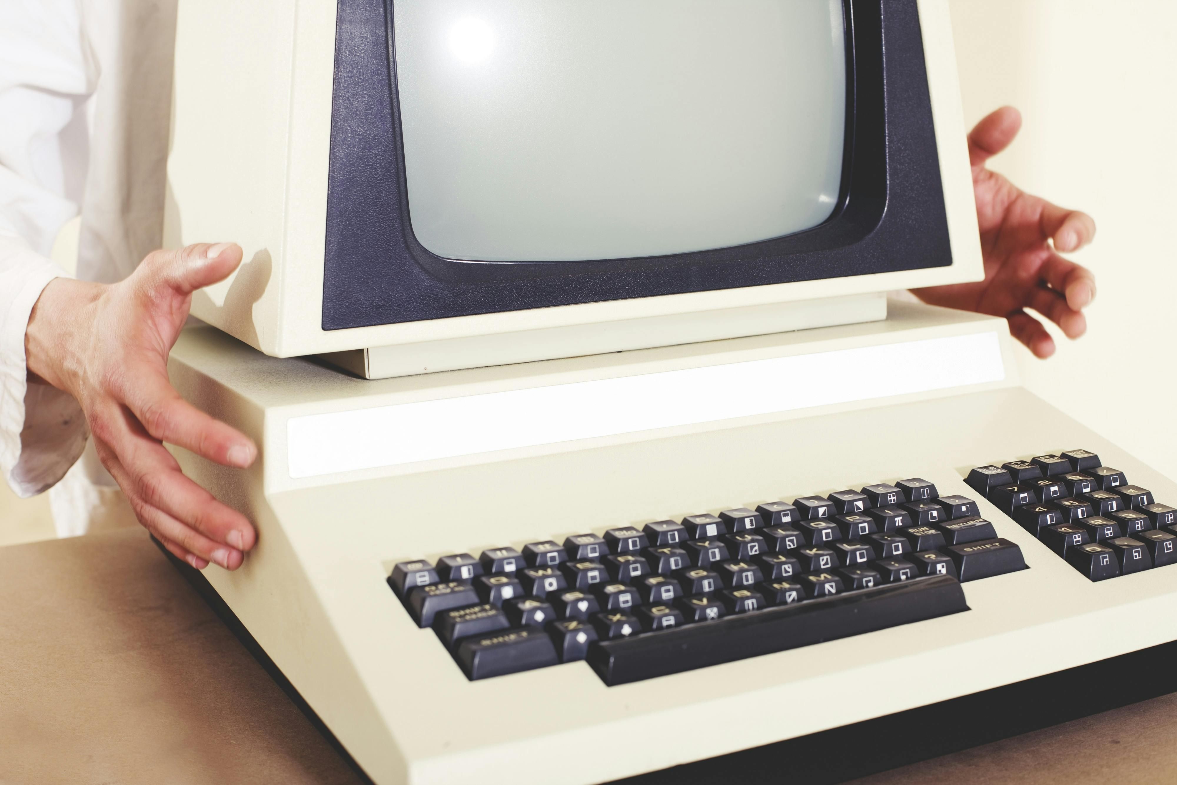 An man holds an old desktop computer from the 1980s.