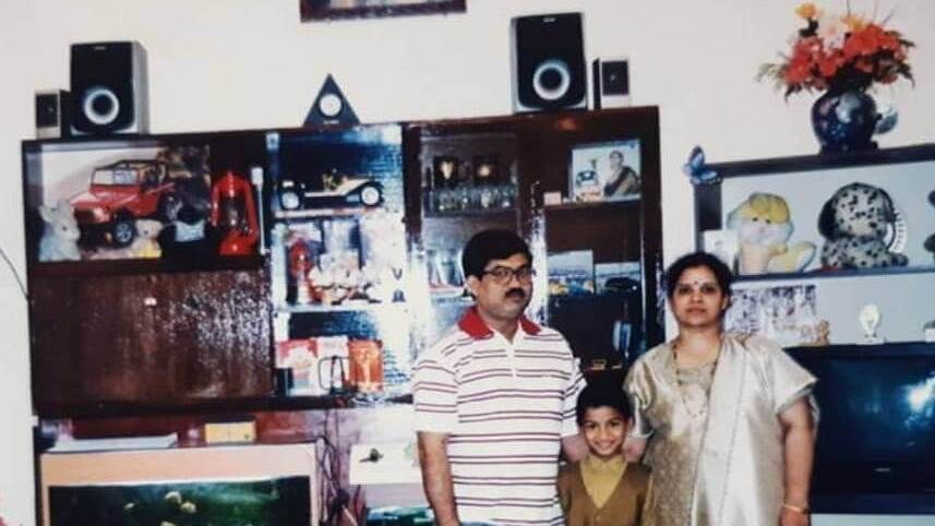 A family photo showing Karkera with his parents at their residence, with bookshelf speakers in the backdrop