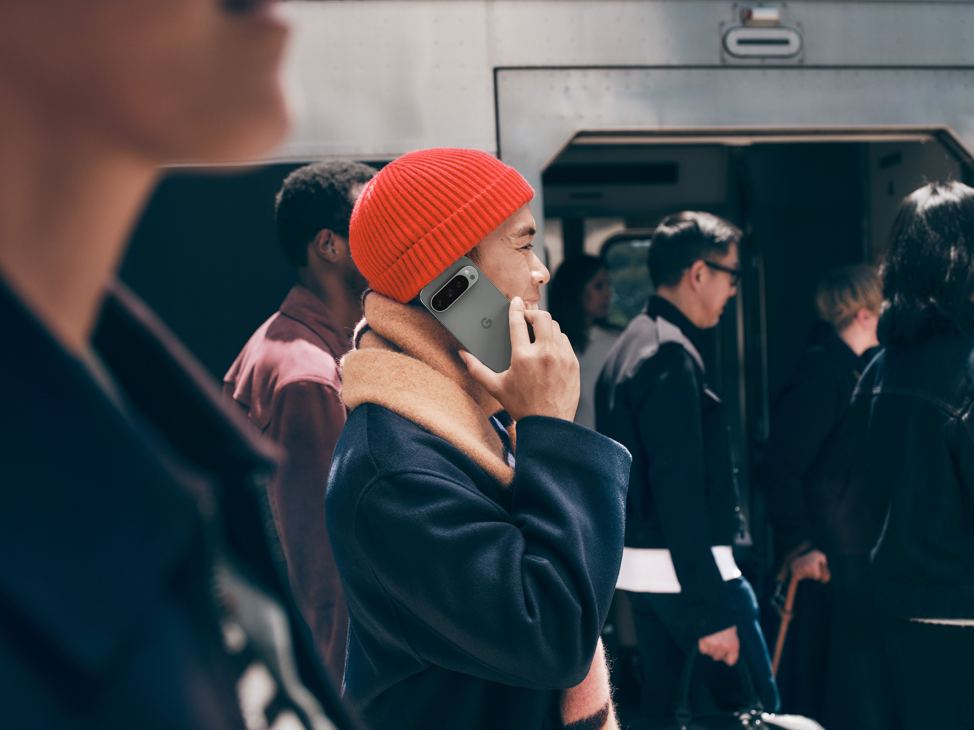 A person wearing a beanie talking on the Pixel 9 Pro while walking down a street.