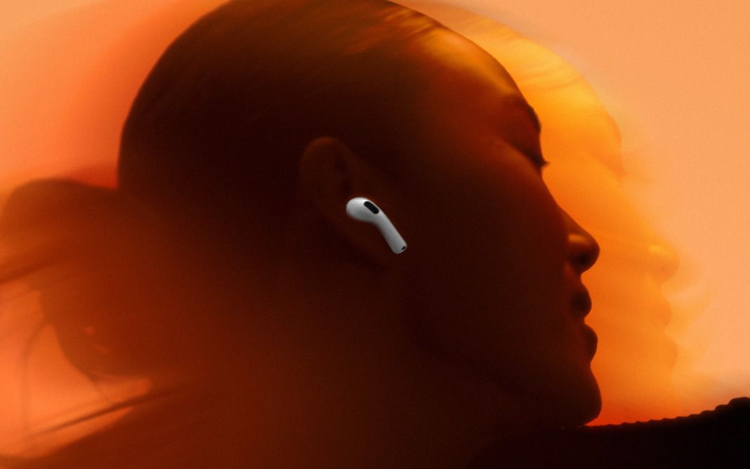 A woman wearing AirPods over an orange background.