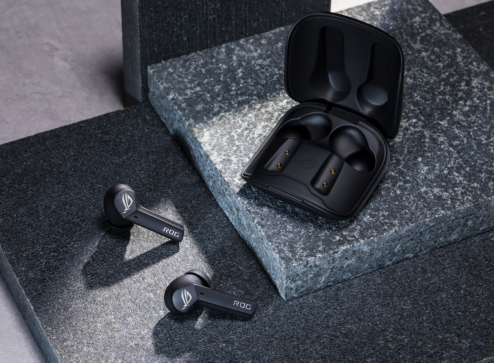 Asus ROG Cetra true wireless in-ear headphones sitting on a slab of granite with their wireless charging case