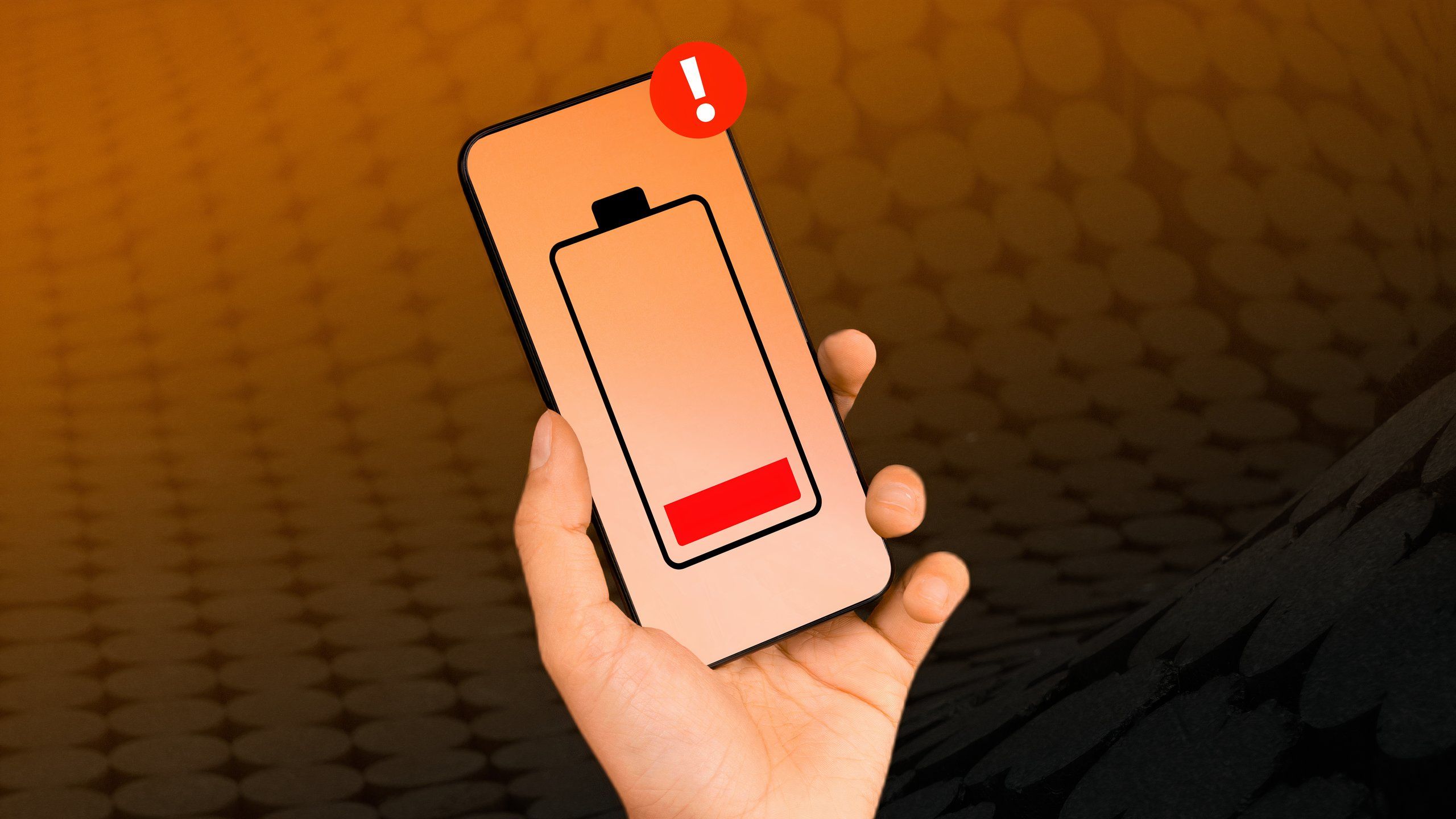 A hand holding a smartphone with a low battery icon in the center.