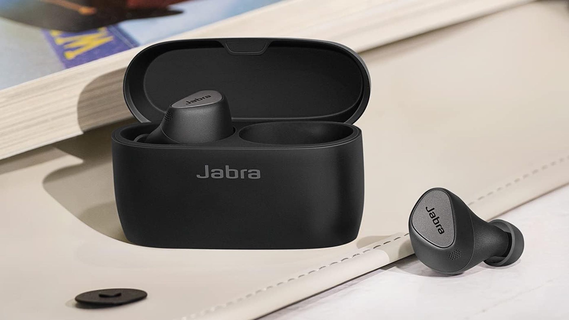 A Jabra Elite earbud alongside its case on a desk.