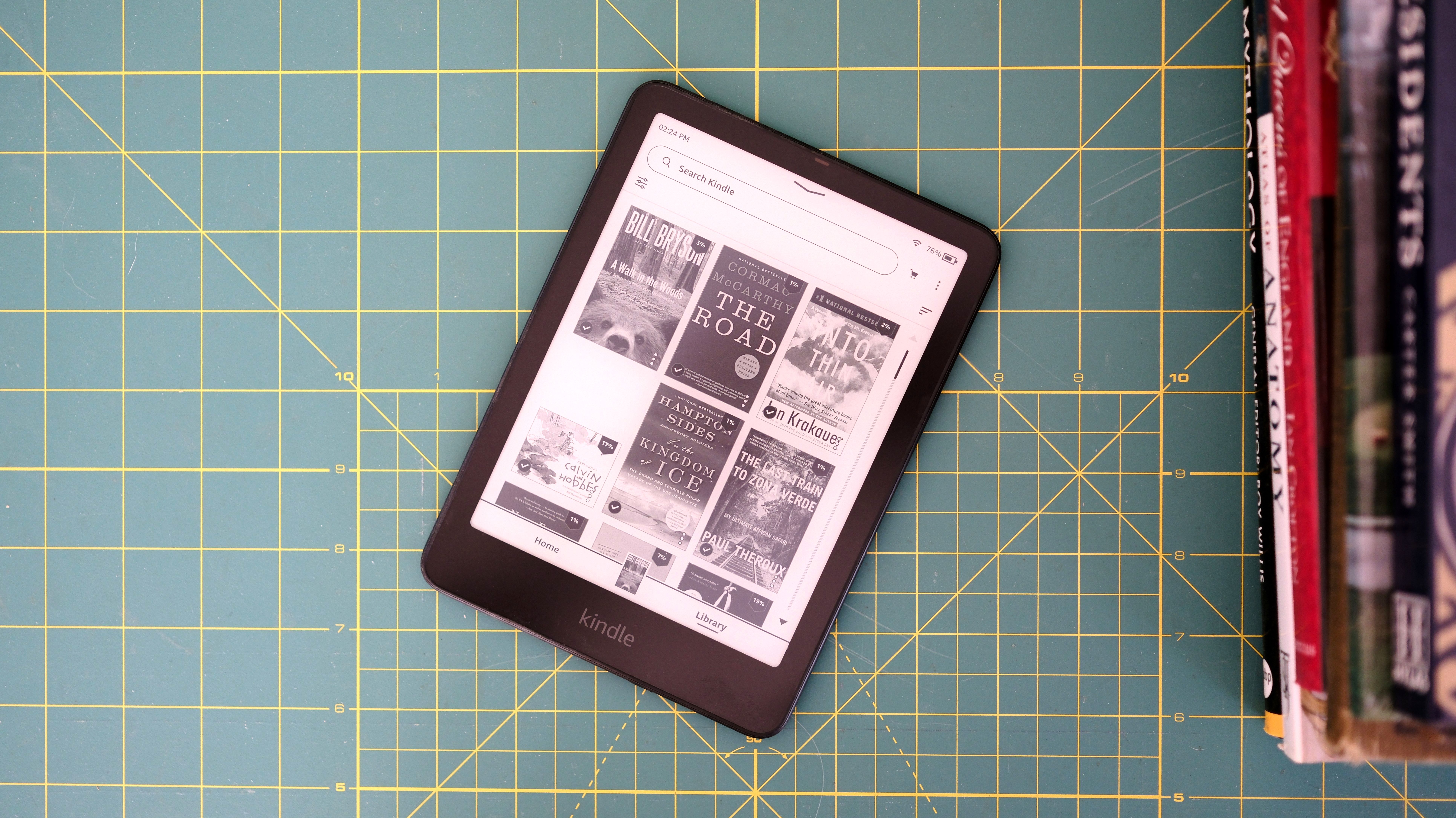 Kindle Paperwhite (2024) on table next to stack of books showing library screen