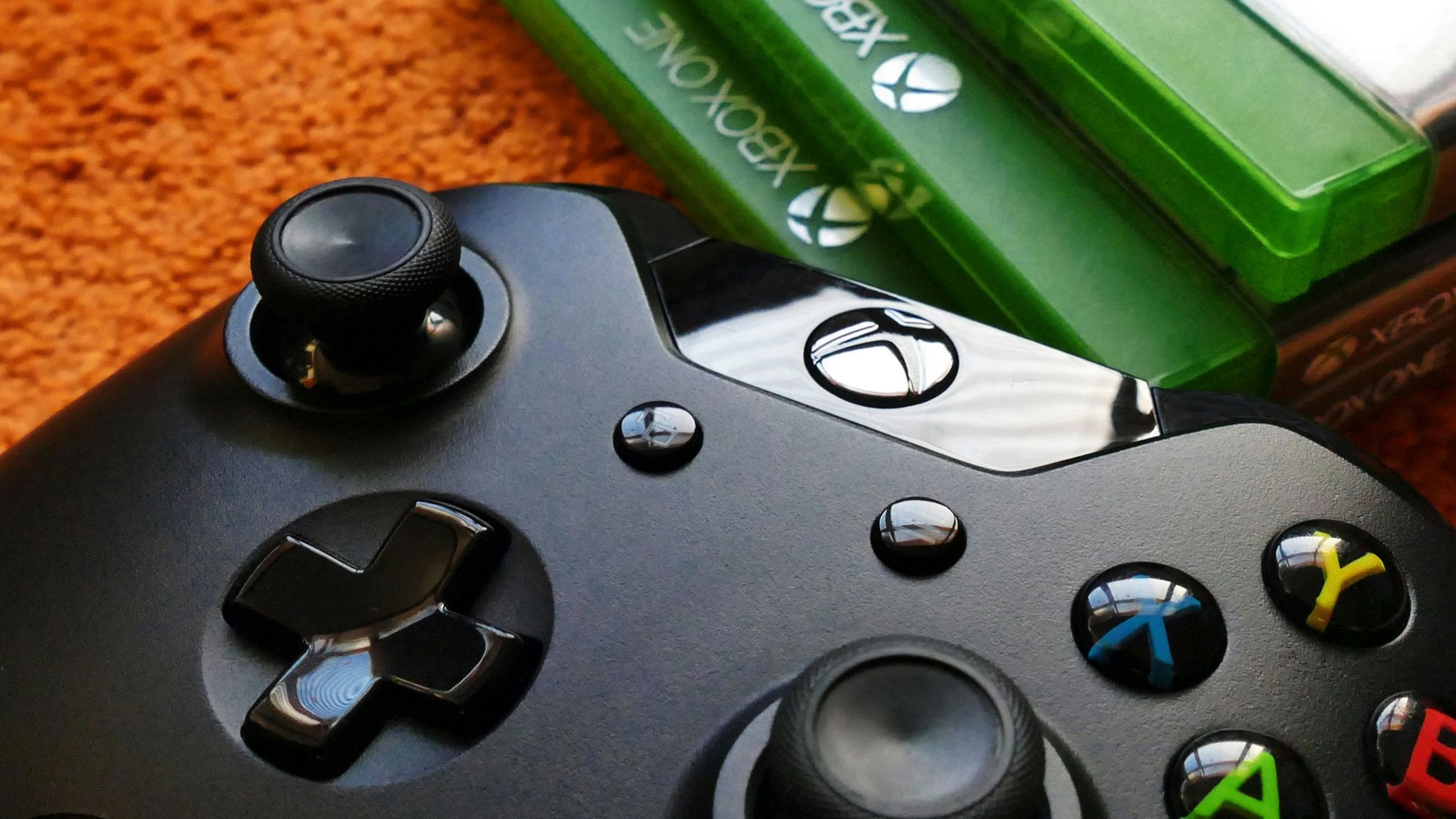 Close up of a black xbox controller next to a stack of Xbox One games