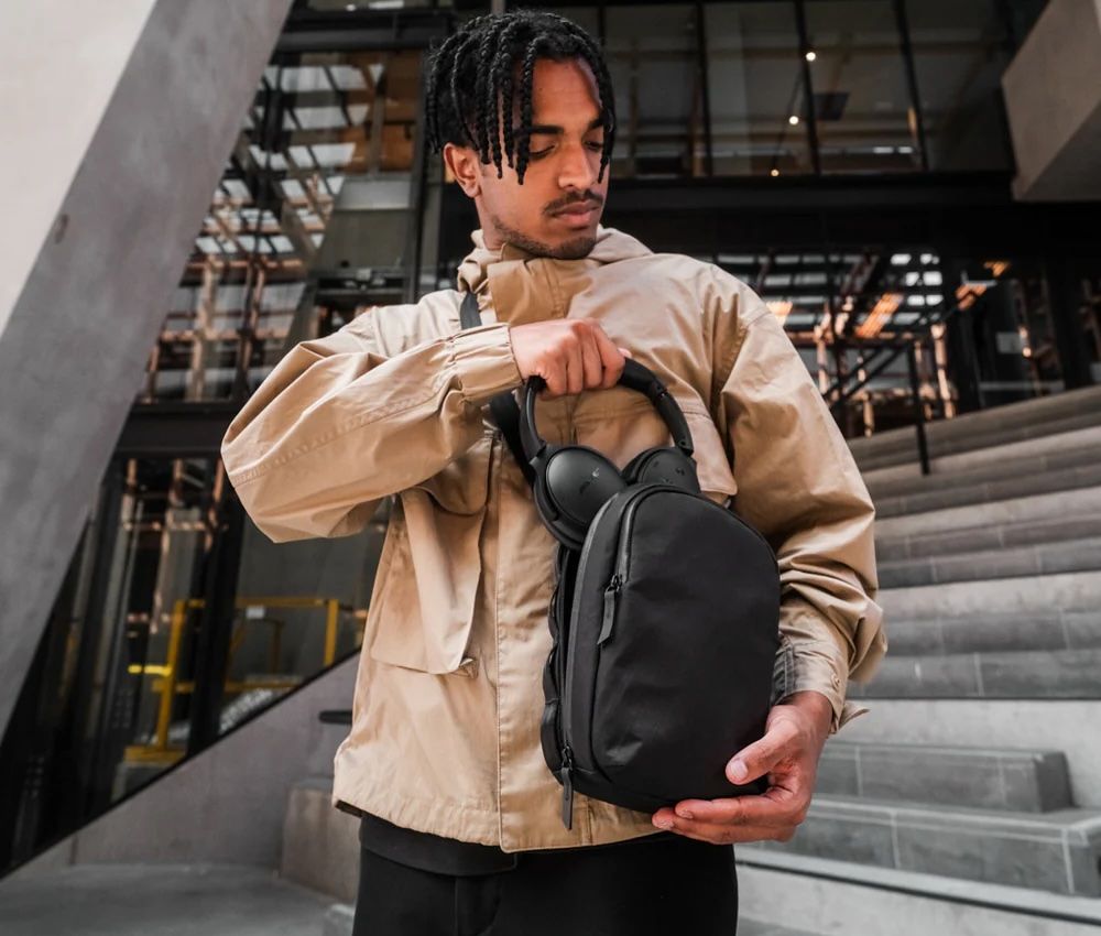 Alpaka Metro Sling Max in black and guy in tan jacket with black headphones 