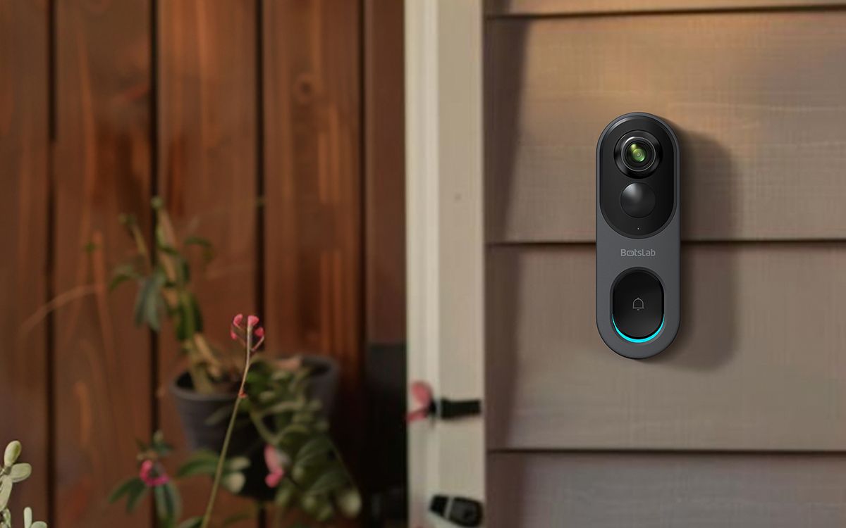 A grey video doorbell against a grey house with a wooden door