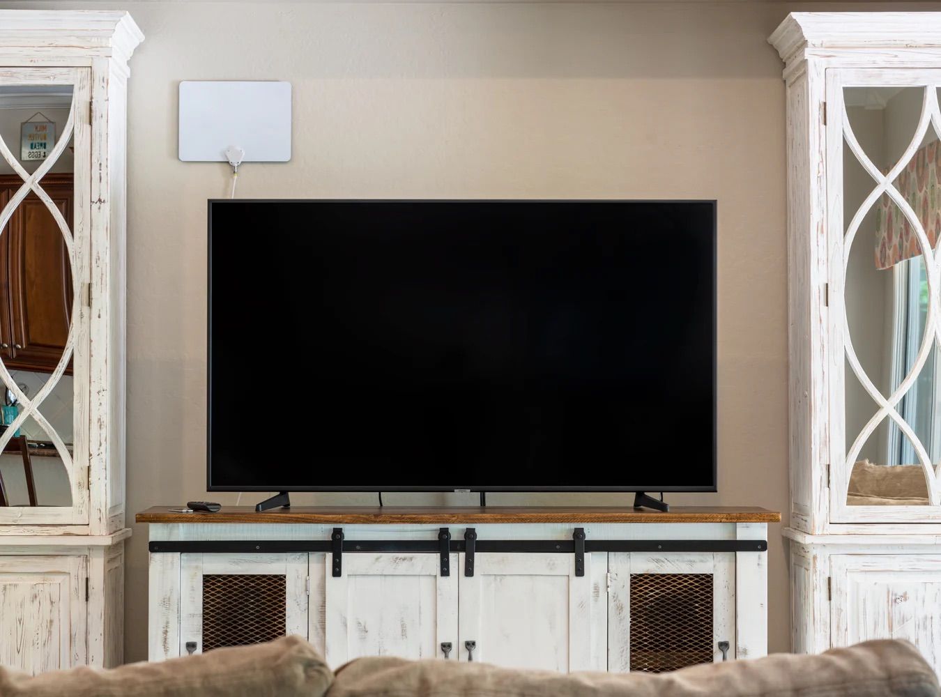 A television in a living room with a white OTA antenna mountd above it