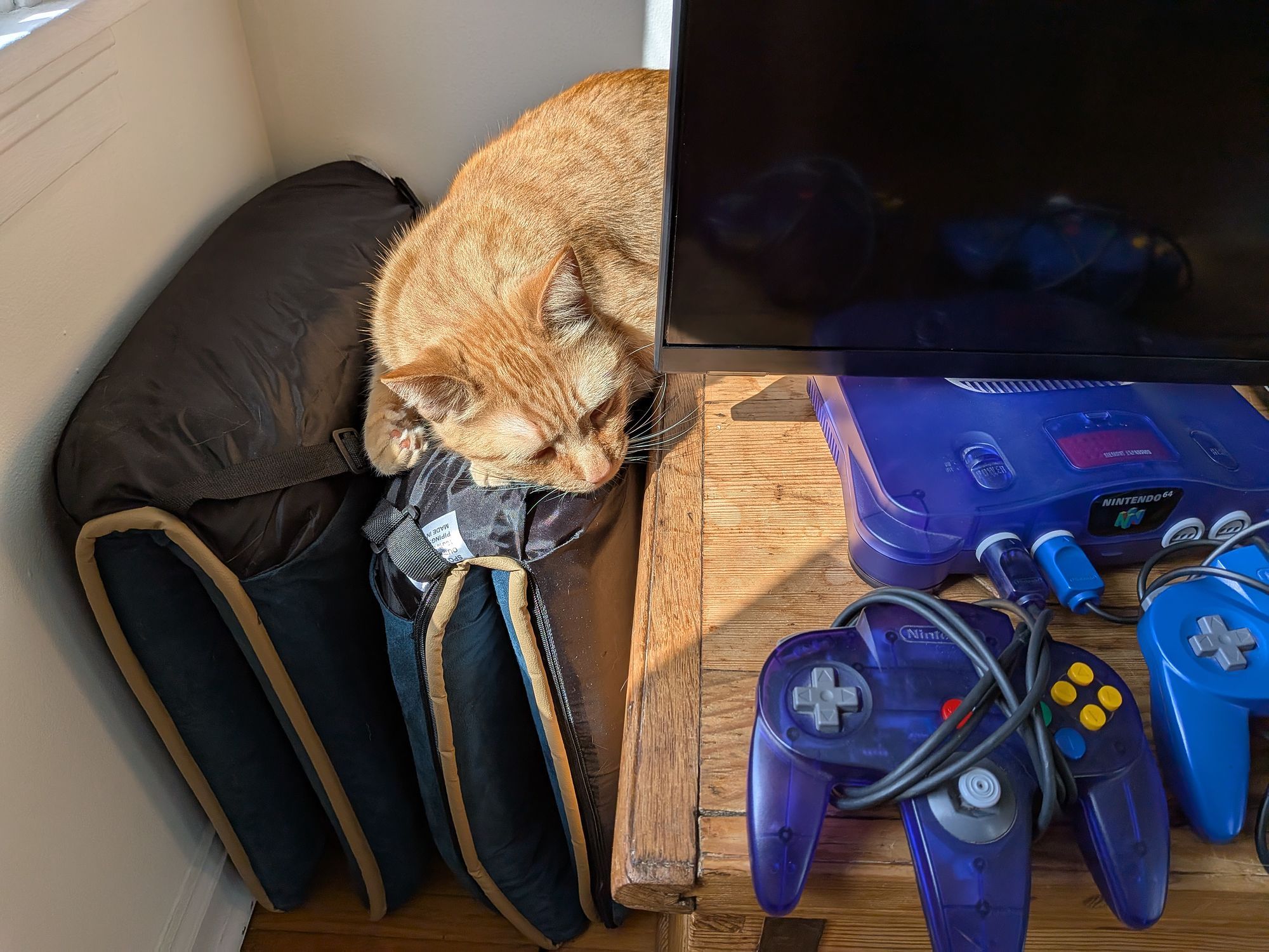 An orange cat sneaking up on a Nintendo 64.