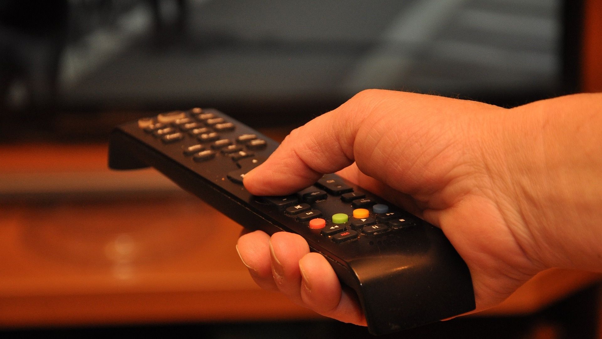 a person holding a remote infront of a tv and table