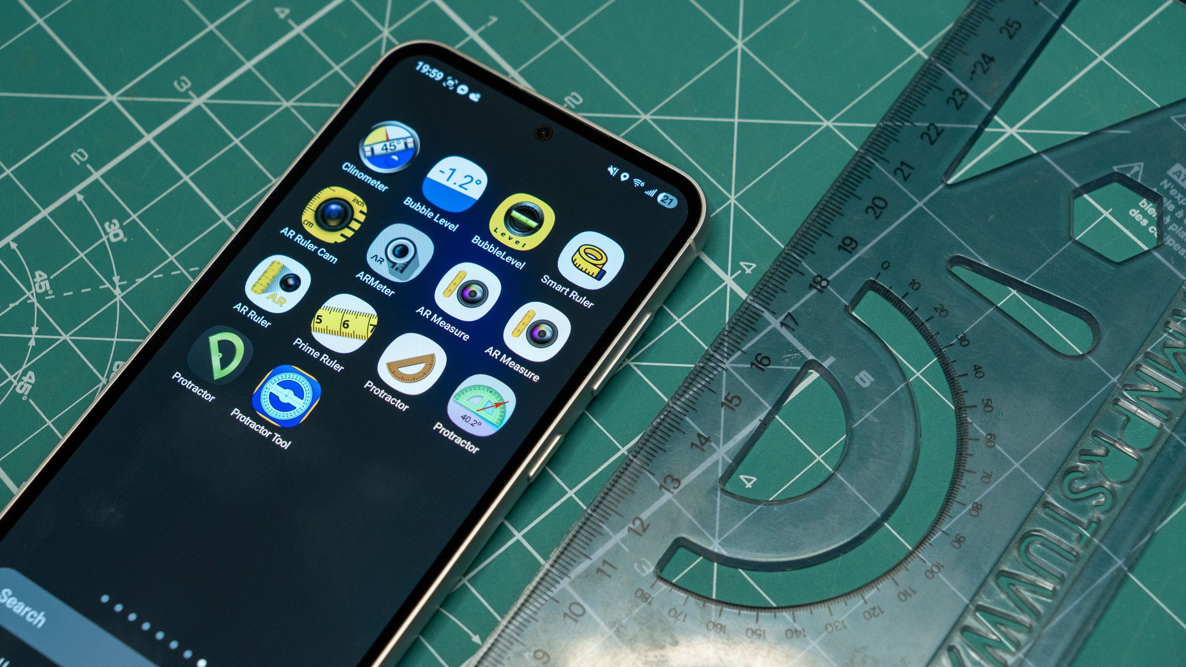 a smartphone displaying icons for tools apps next to a plastic ruler on a green mat
