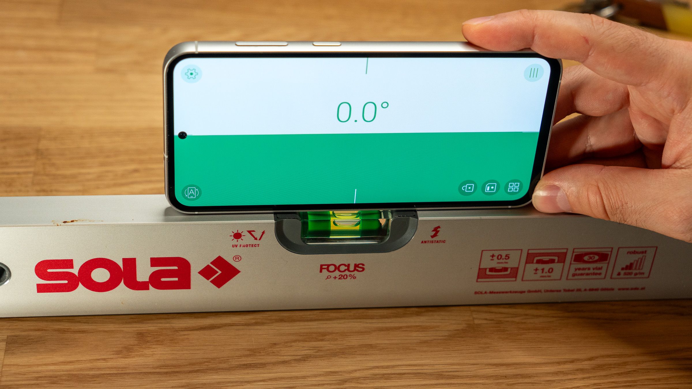 a phone displaying a level app over a spirit level on a wooden table
