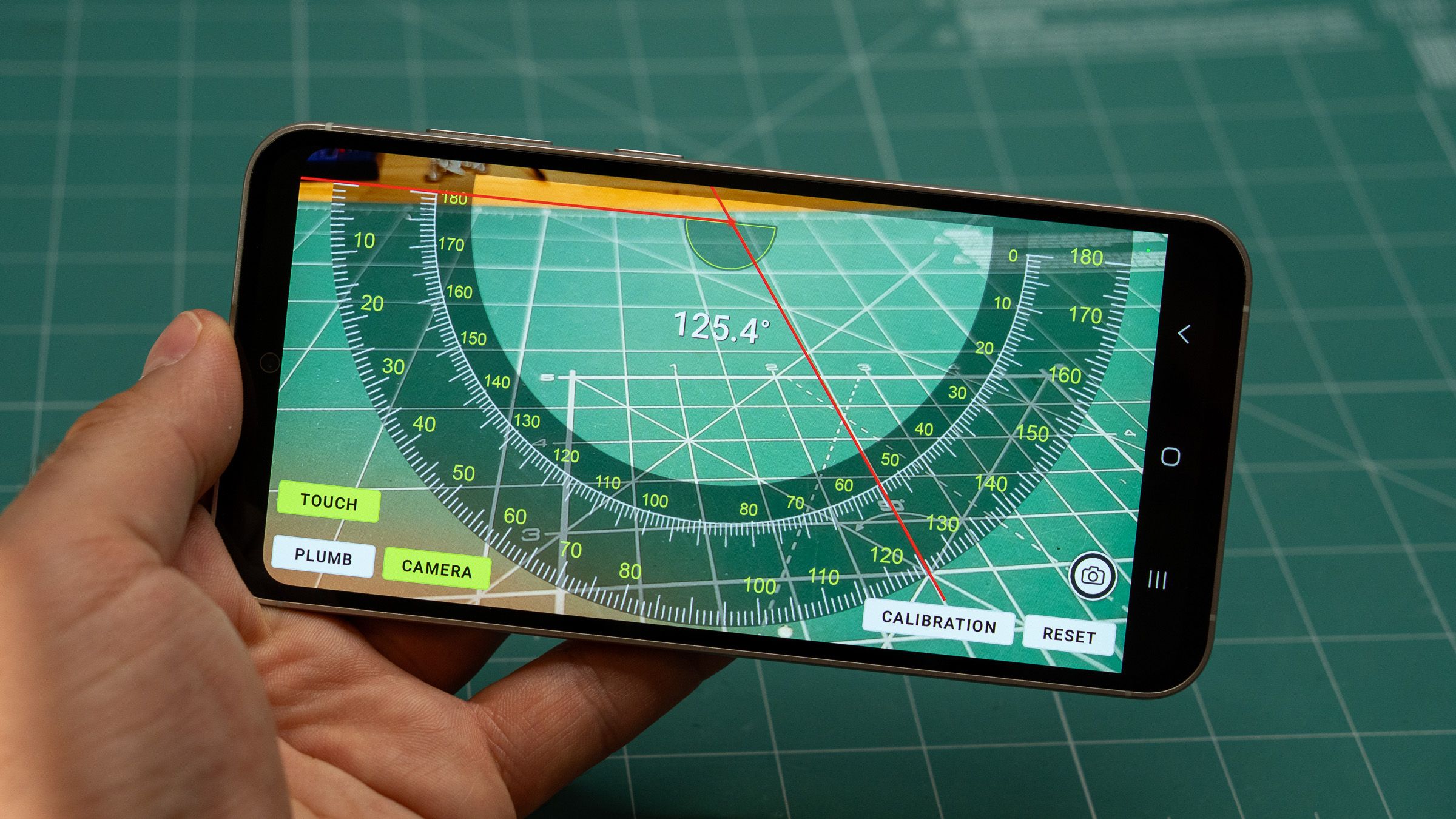 a phone in hand displaying a protractor app on a green mat
