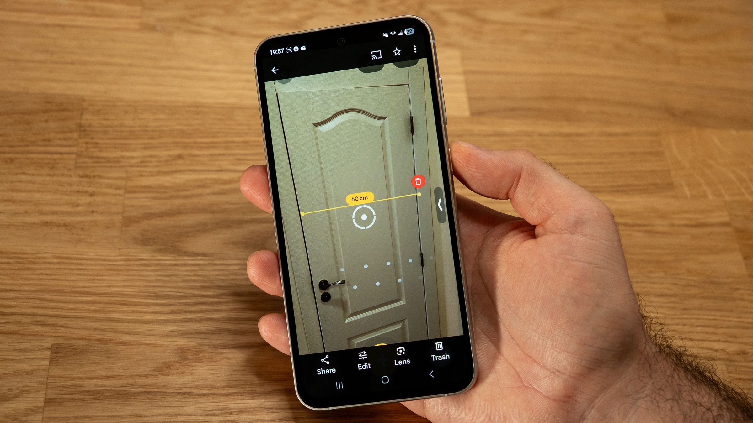 a phone in hand displaying an AR measurement app on a wooden table