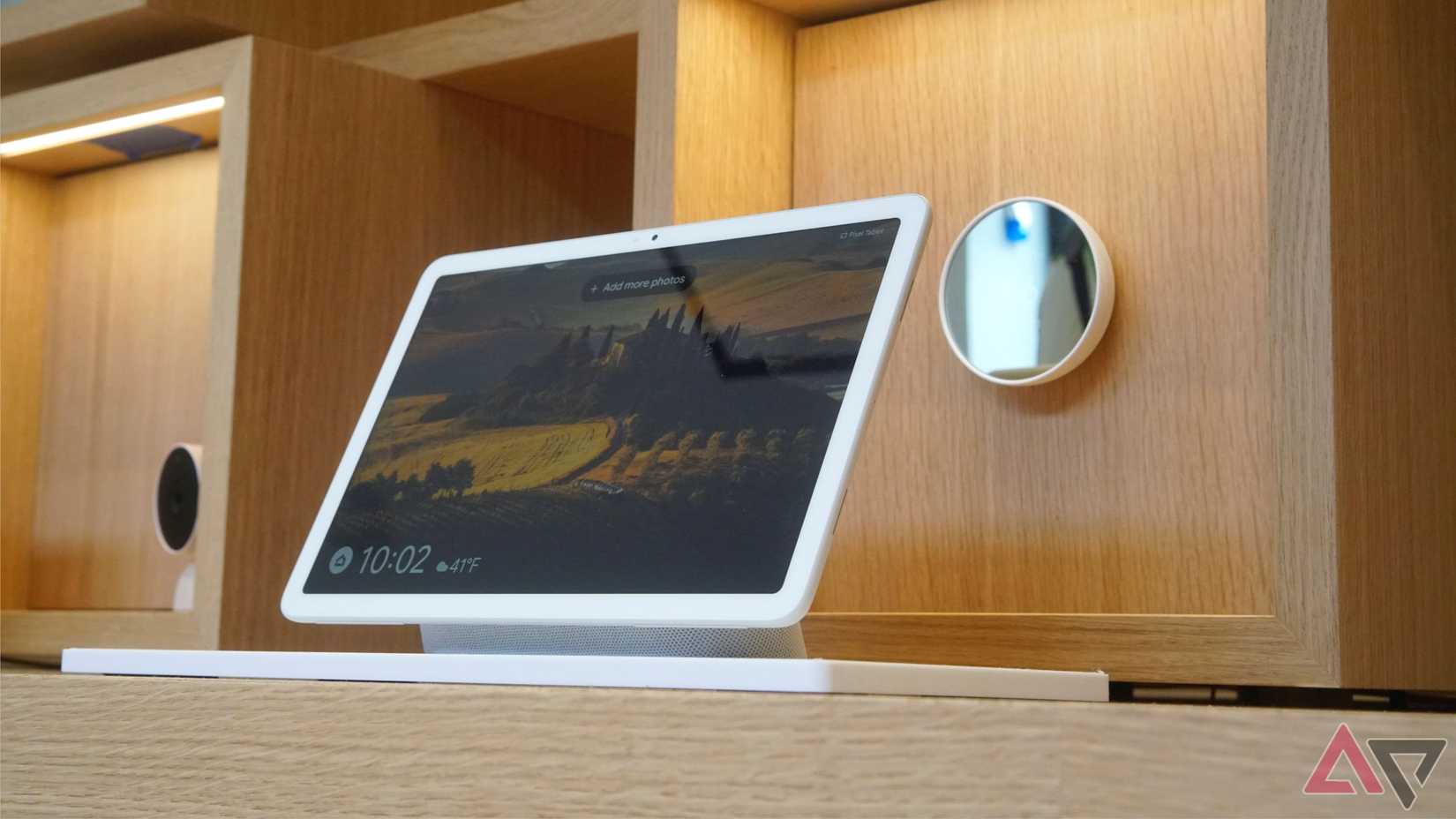 A Pixel Tablet sitting on a table with a Nest Thermostat on a wall in the background.