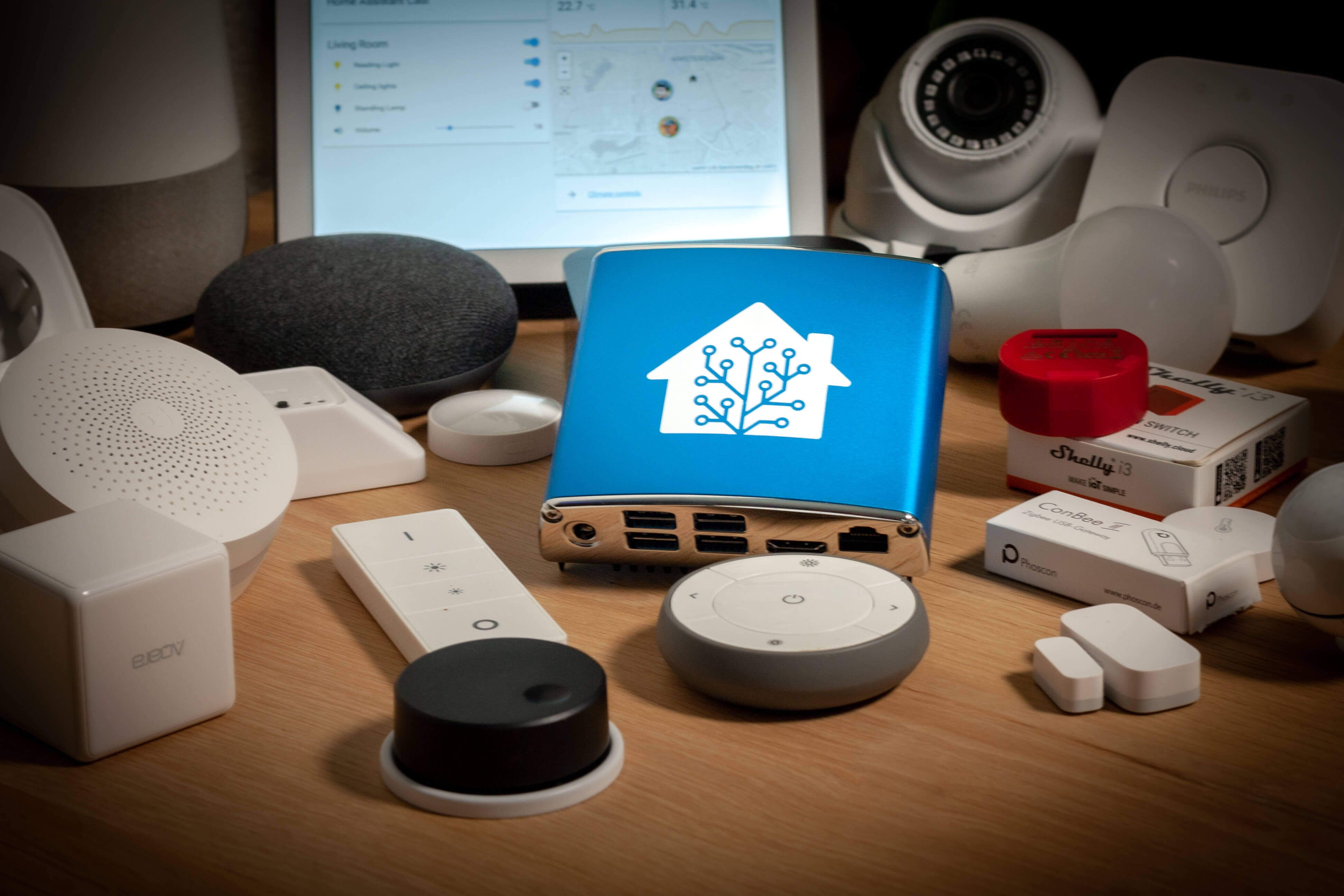 A Home Assistant Blue controller on a table, next to a variety of smart home devices.