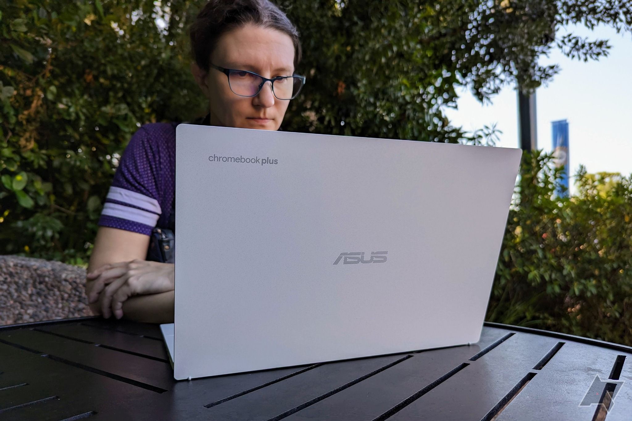 An Asus Chromebook Plus CX34 being used by a person sitting on a brown table outside
