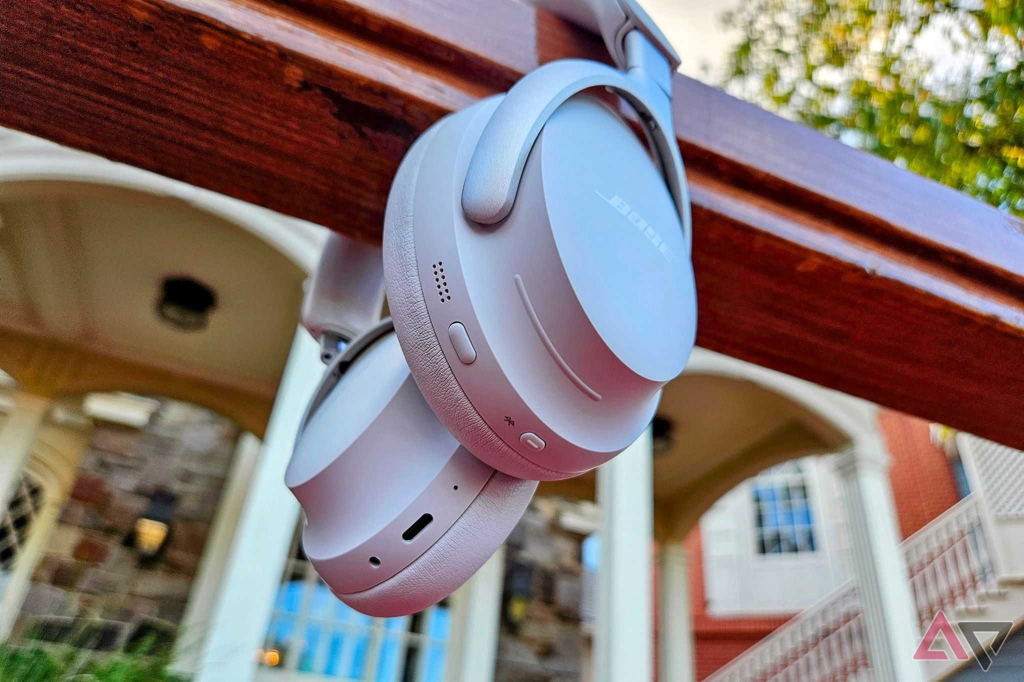 White Bose QuietComfort Ultra headphones hanging on a porch railing outside.