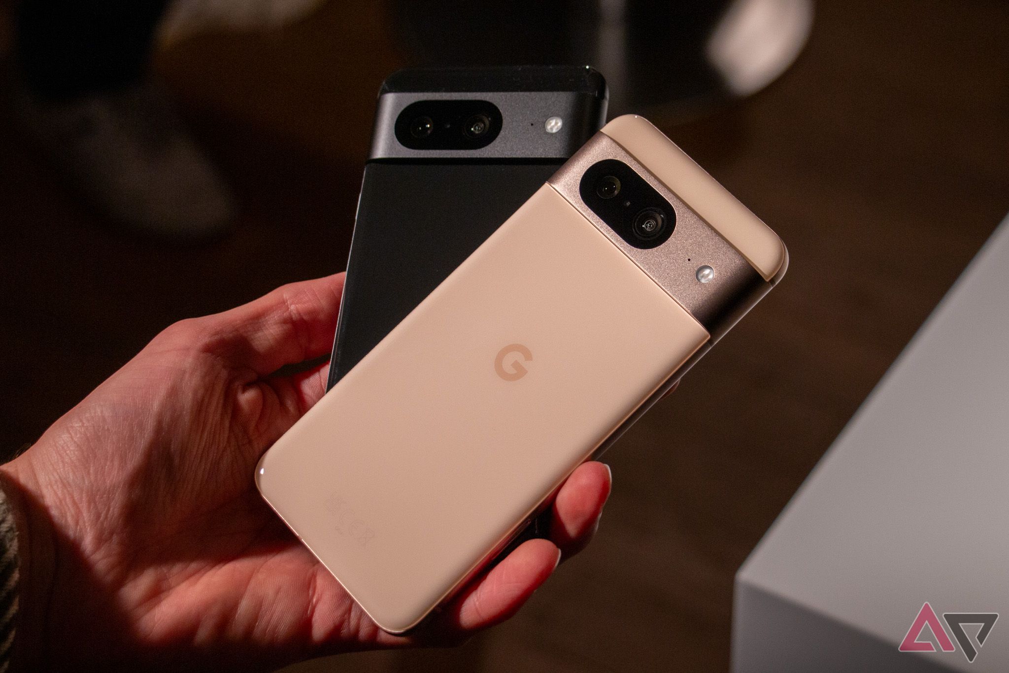 A hand holding two Google Pixel 8 phones, one in black and one in peony rose.