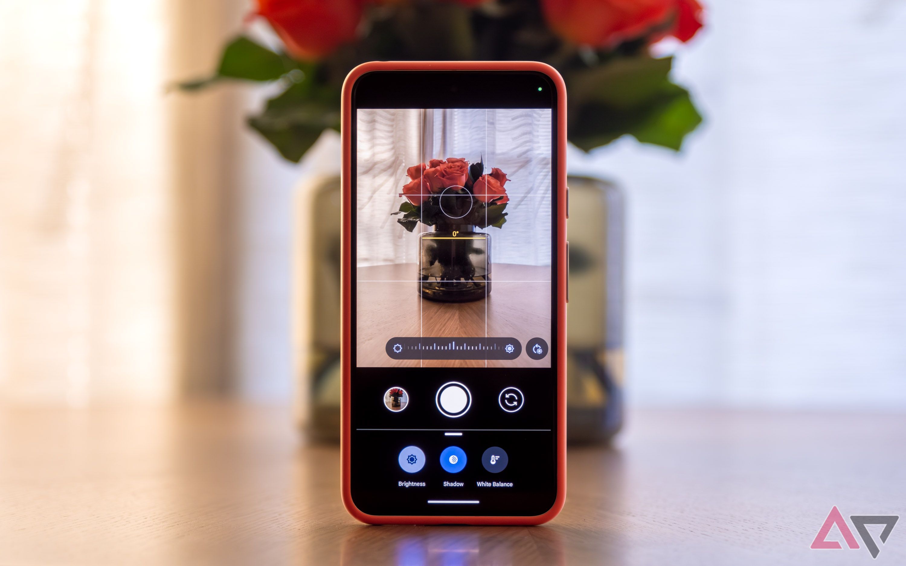 The Camera app on a Pixel phone resting upright on a table with a vase of flowers.