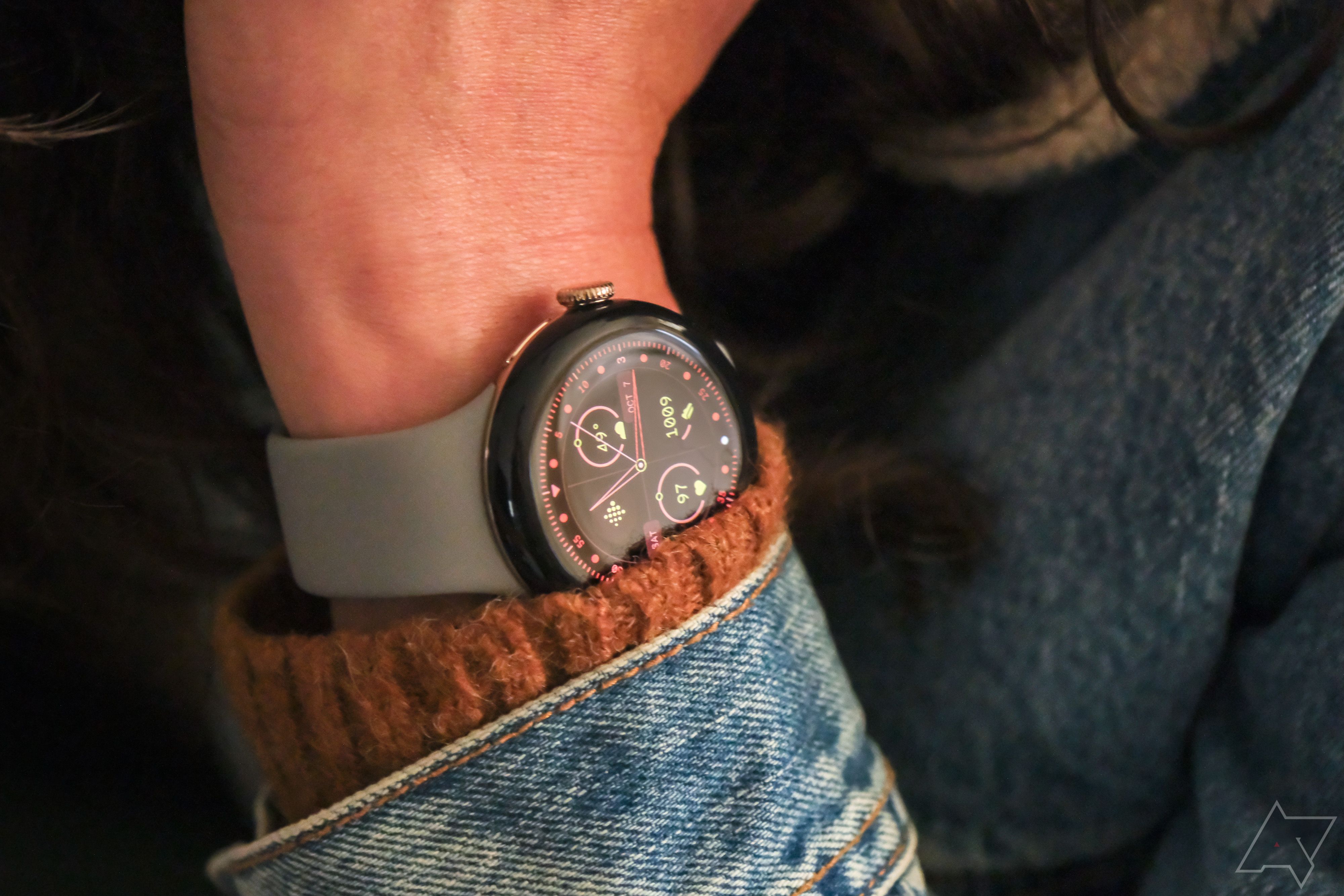 A person wears the Google Pixel Watch 2 with a denim jacket and wool sweater.