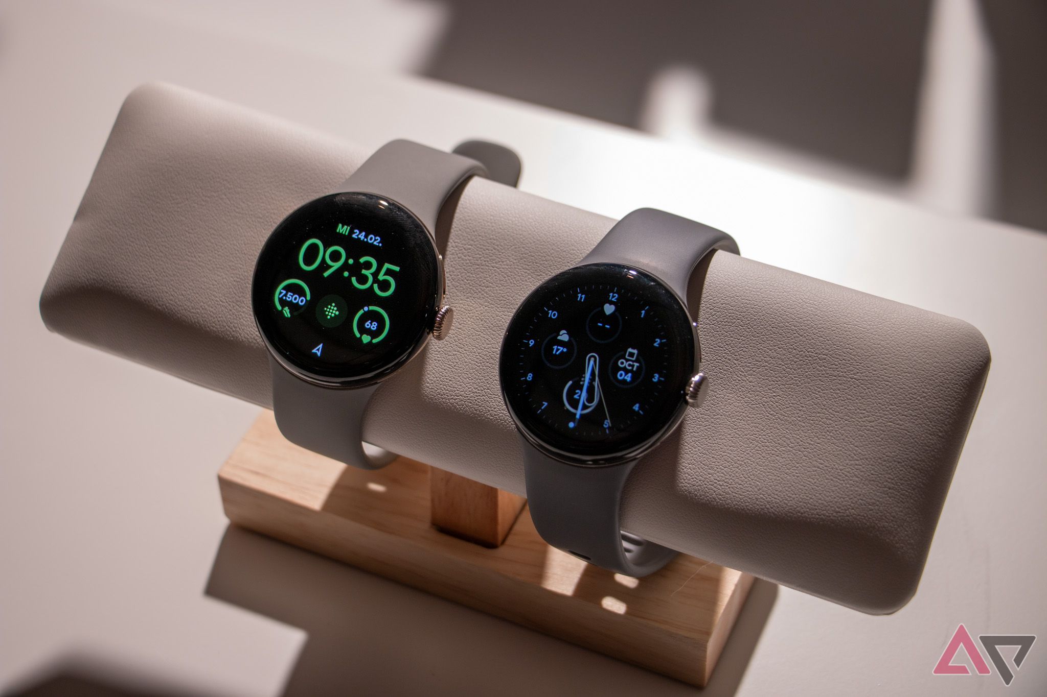 The Google Pixel Watch 2 next to the Google Pixel Watch 1 on a faux leather watch stand