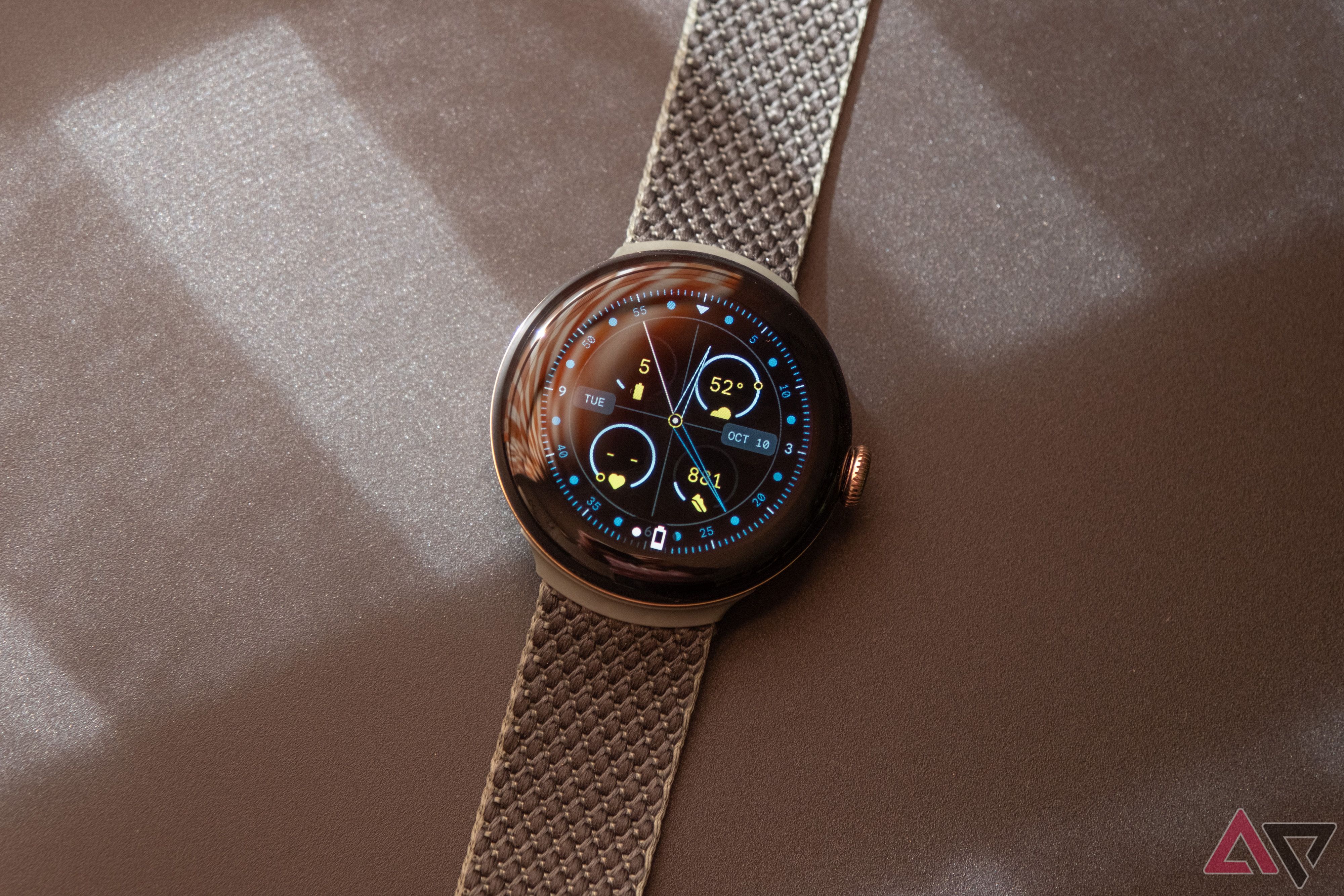 A Google Pixel Watch rests atop a tan textured surface