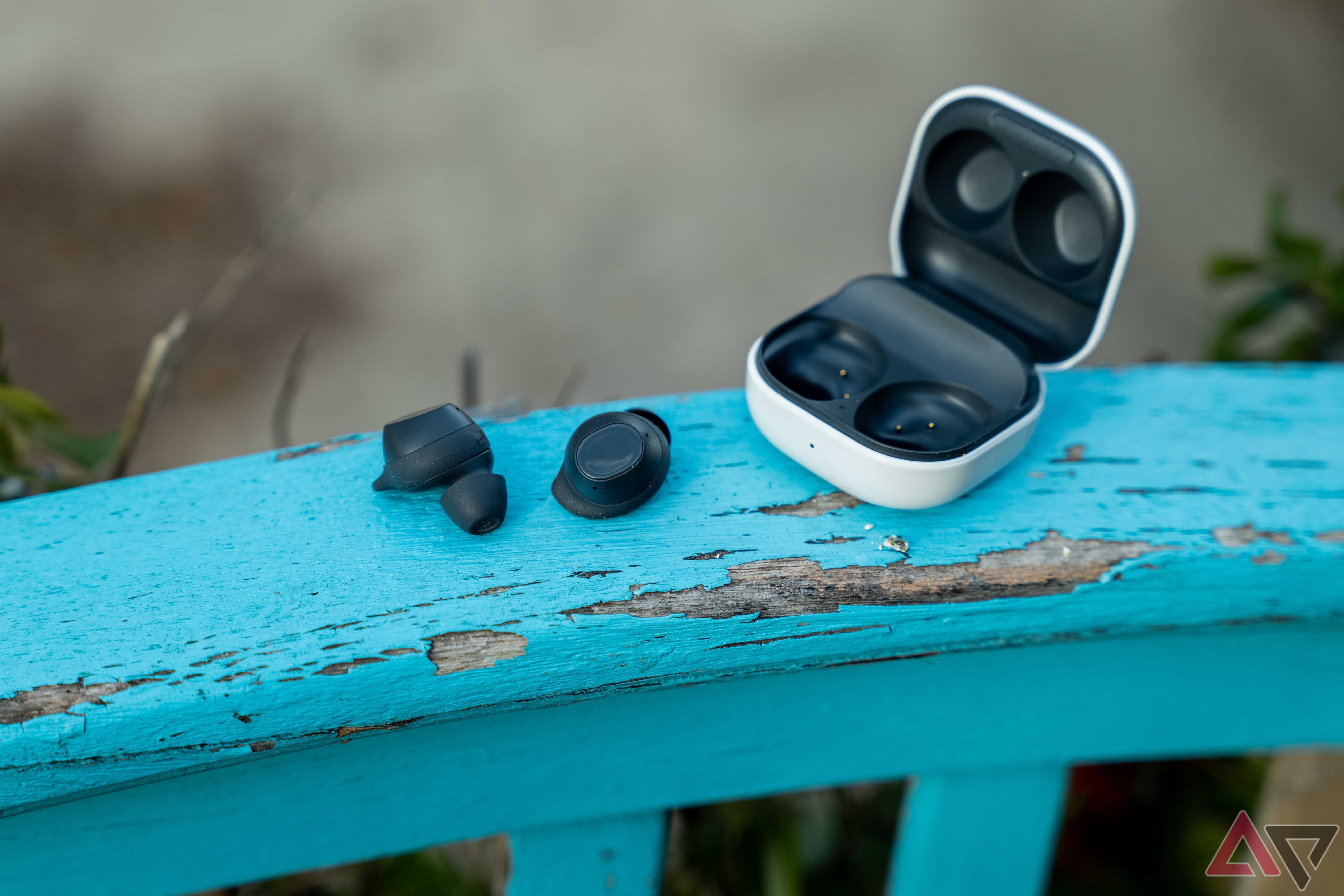 The Galaxy Buds FE out of the open case on a blue rail