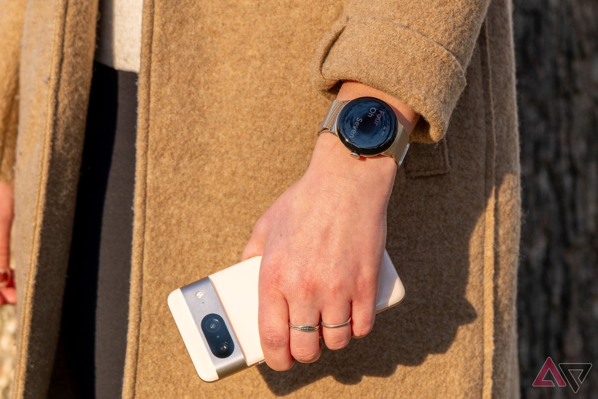 A person wearing a Google PIxel Watch on their wrist and holding a Google Pixel 8 phone.