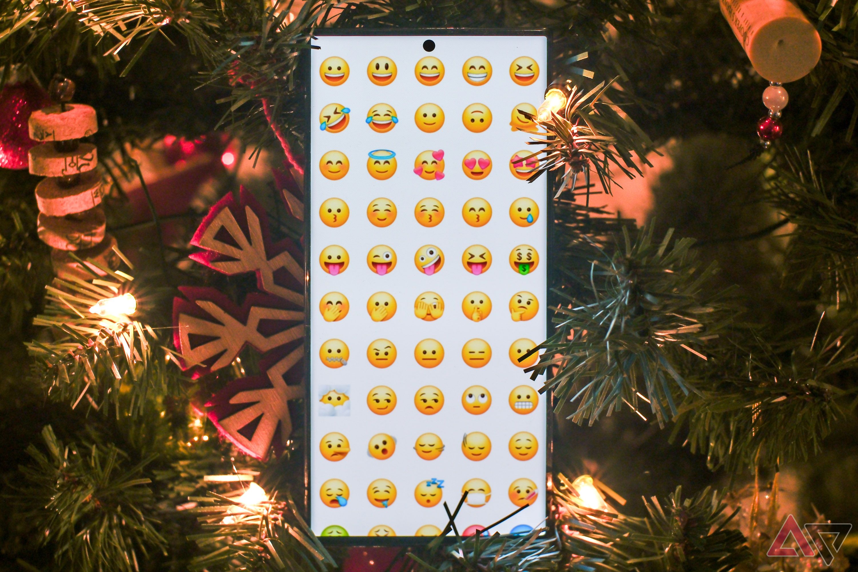 A smartphone showing a grid of emojis, surrounded by holiday decorations