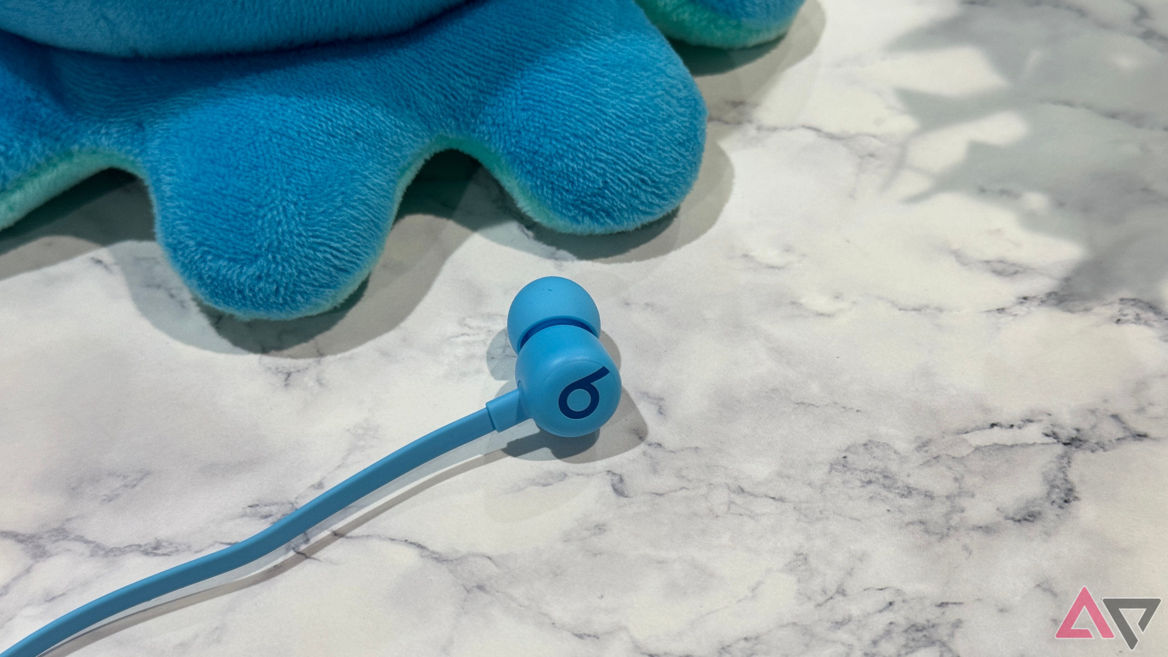 Beats Flex earbud laying down next to a plushie