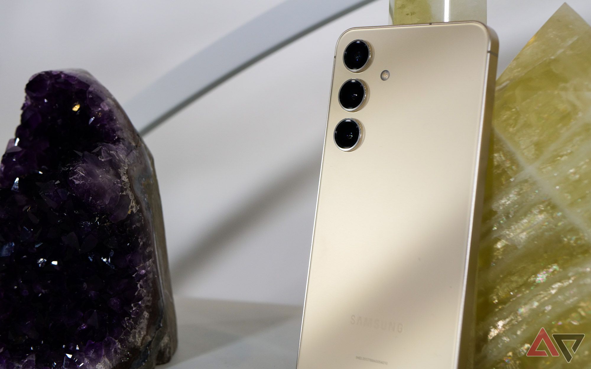 A cream-colored Galaxy S24 next to yellow and purple stones.