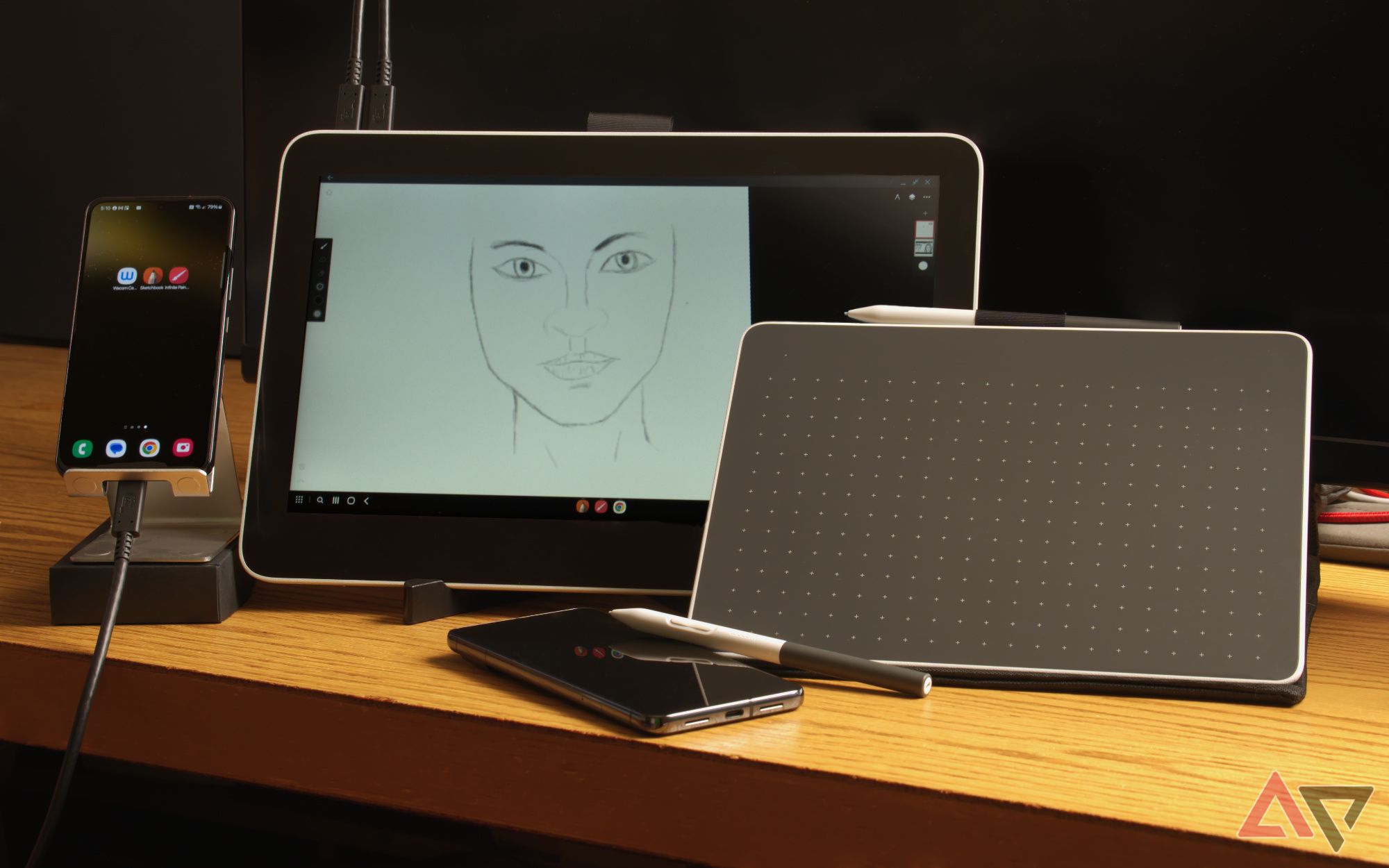 Wacom drawing tablets propped up on a desk next to phones, one shows a drawing