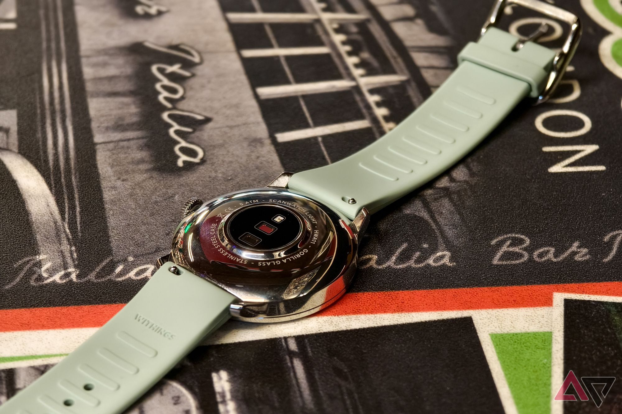 Withings ScanWatch Light in Green, photographed from above at an angle, resting face-down on an Italian restaurant table so that the watch sensors are visible