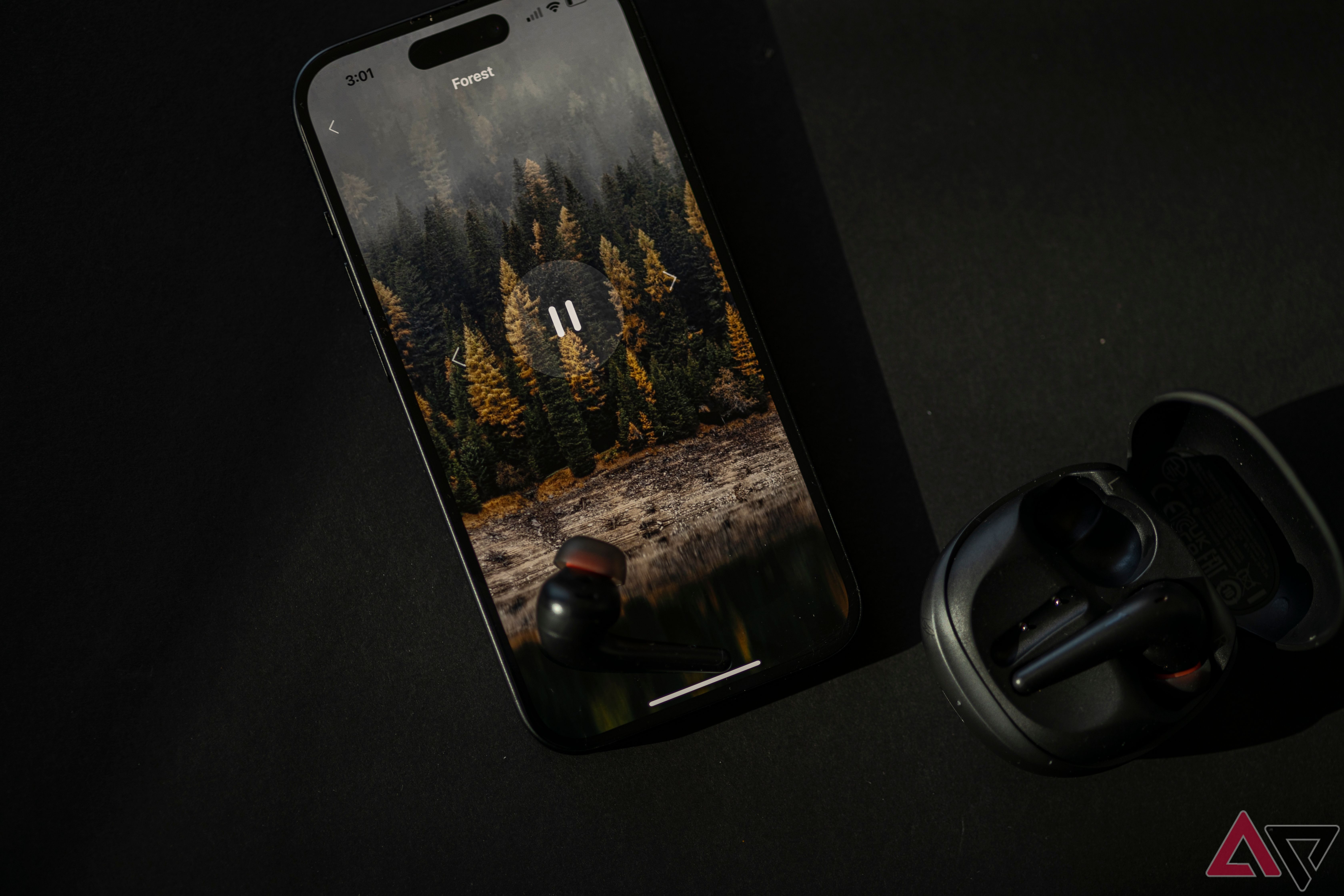 1More Aero earbud sitting on iPhone, open to forest soundscape, with open earbud case nearby