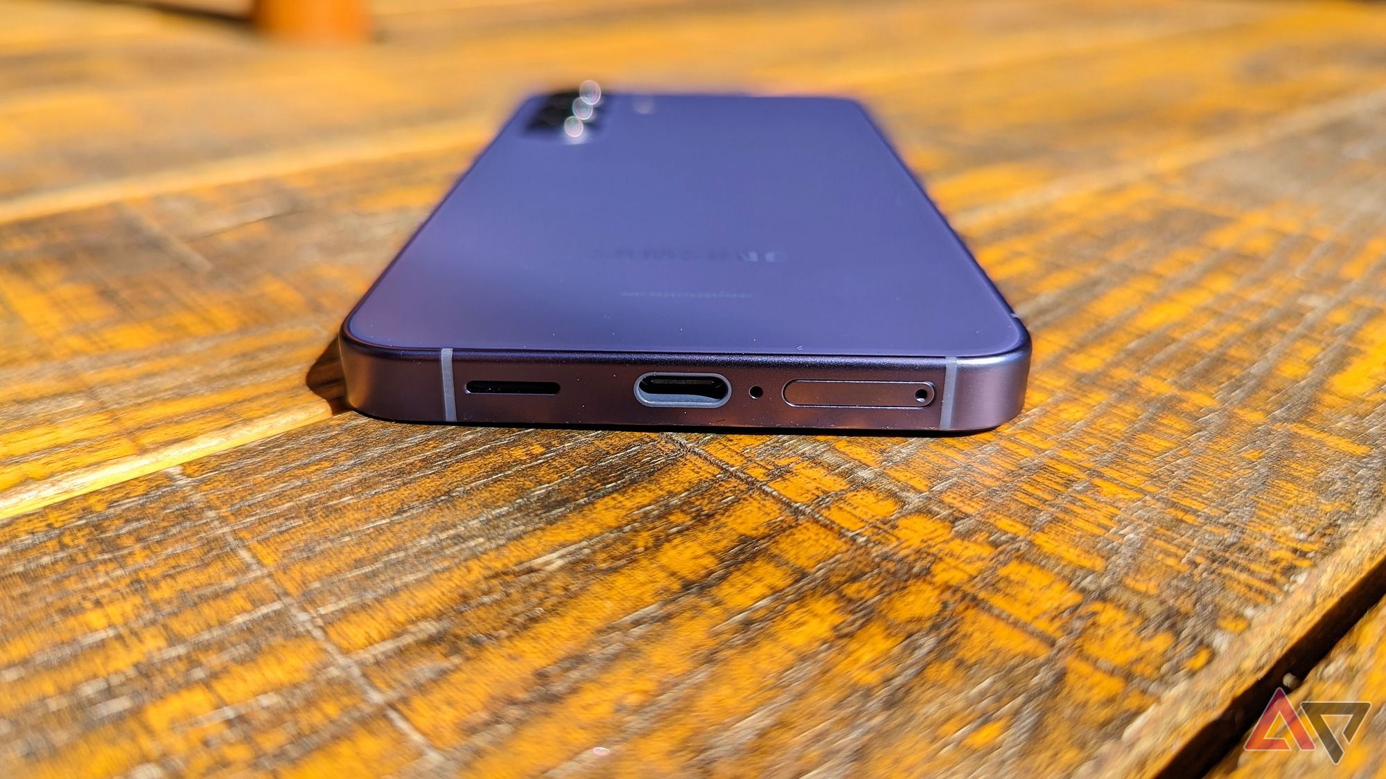 The speaker, USB-C port, and SIM tray on the Samsung Galaxy S24 on a wooden table
