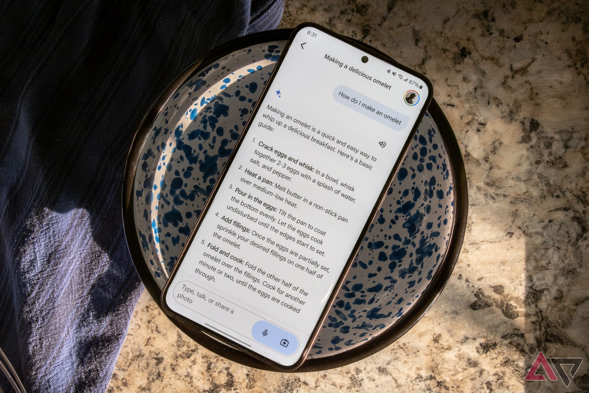 A Samsung smartphone sitting on a mixing bowl, showing a recipe for an omelette in Google Gemini