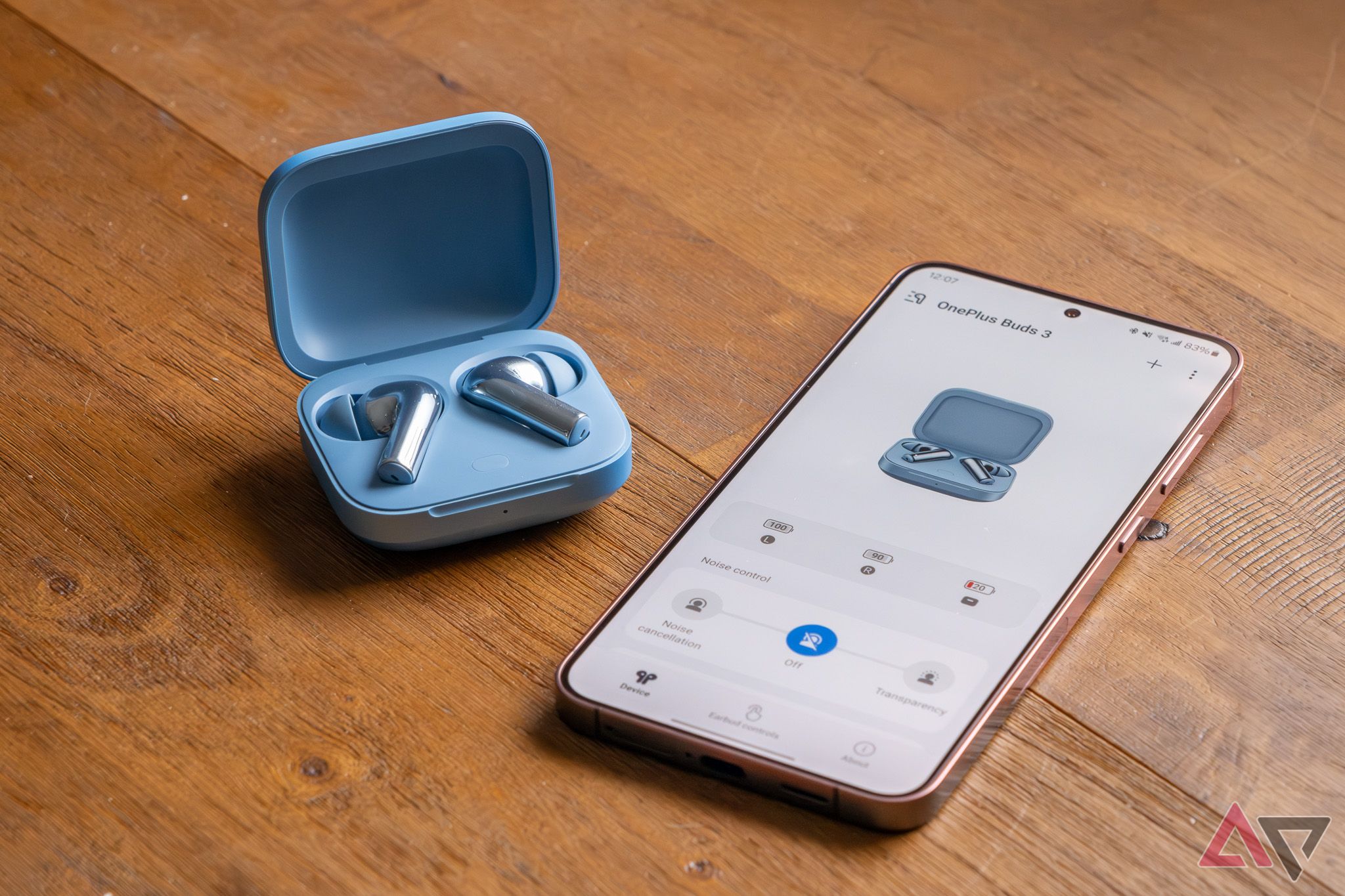 True wireless earbuds in a charging case, next to a smartphone running their companion app