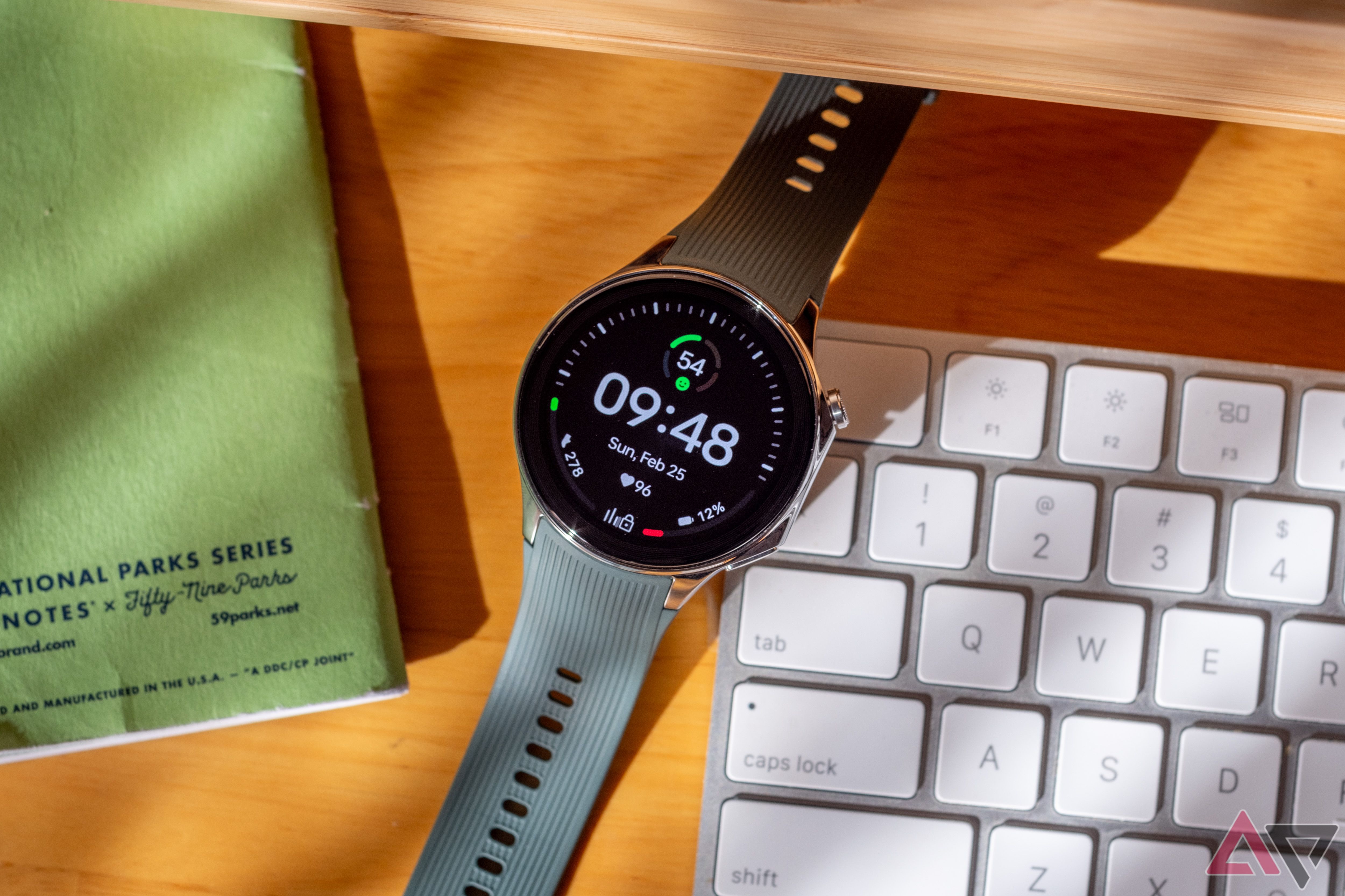 A smartwatch on a desk between a notebook and a keyboard