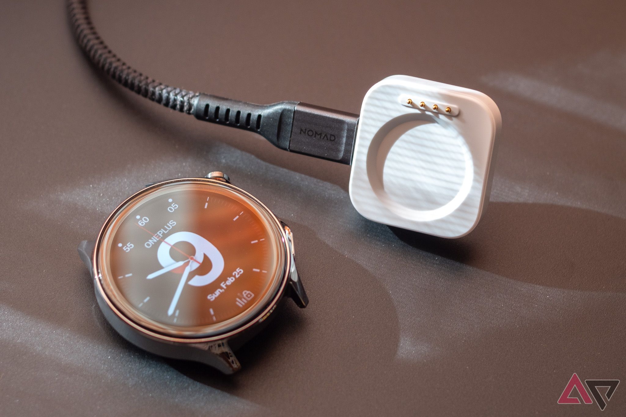 A smartwatch with no band attached, next to its charger