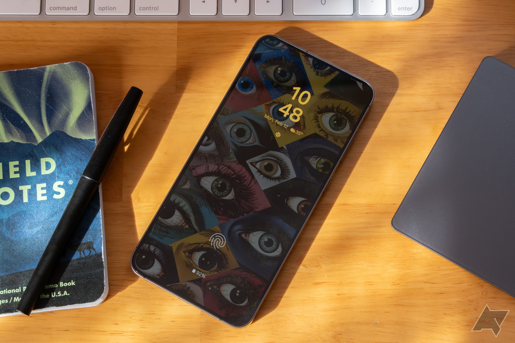 A Samsung phone on a desk, showing a wallpaper featuring many eyes