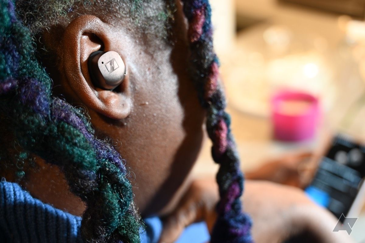 Over shoulder view of African American woman wearing Sennheiser Momentum True Wireless 4 earbuds looking at smartphone