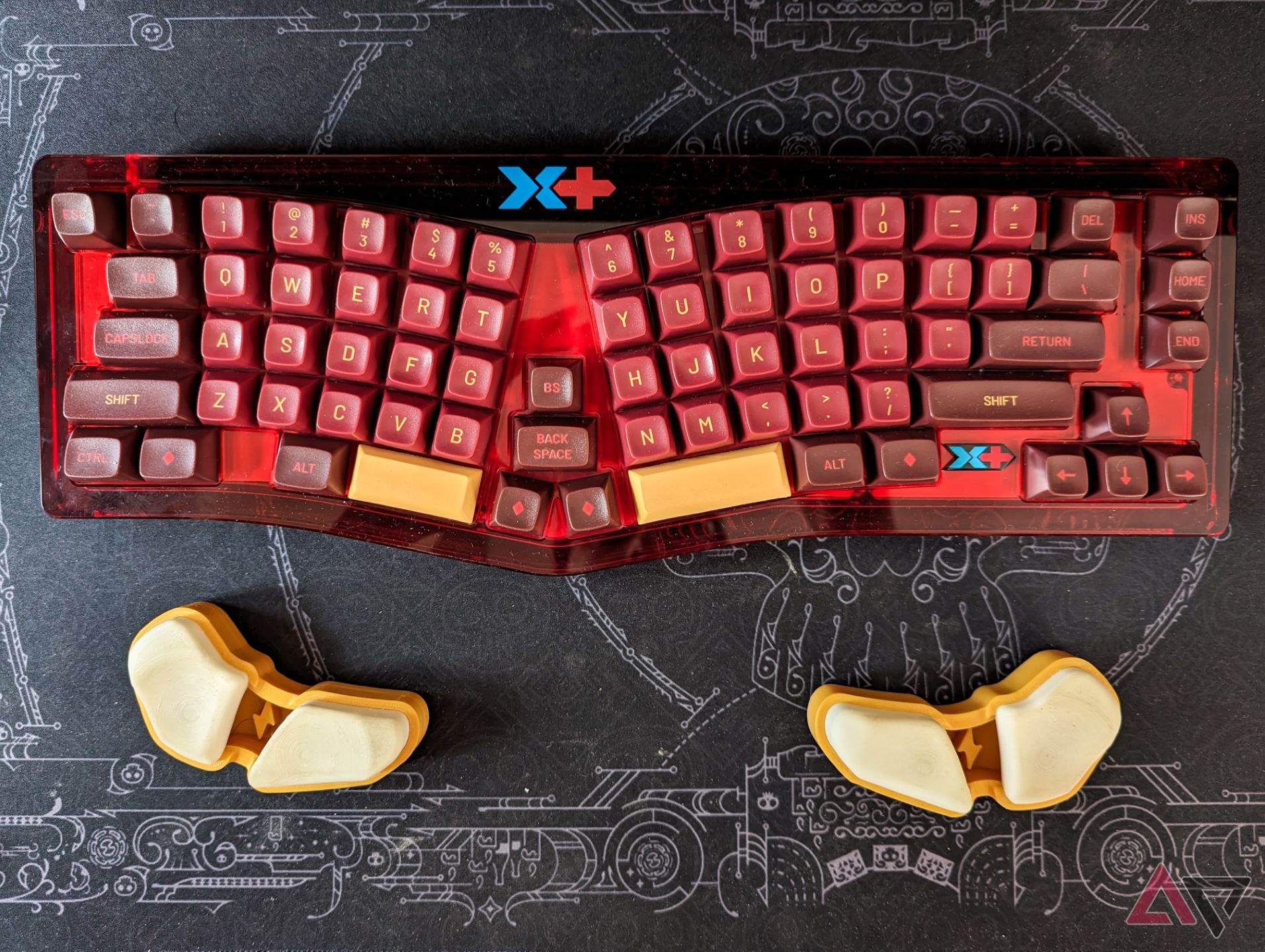 A red acrylic keyboard with red and yellow keycaps to match sitting on a black deskmat