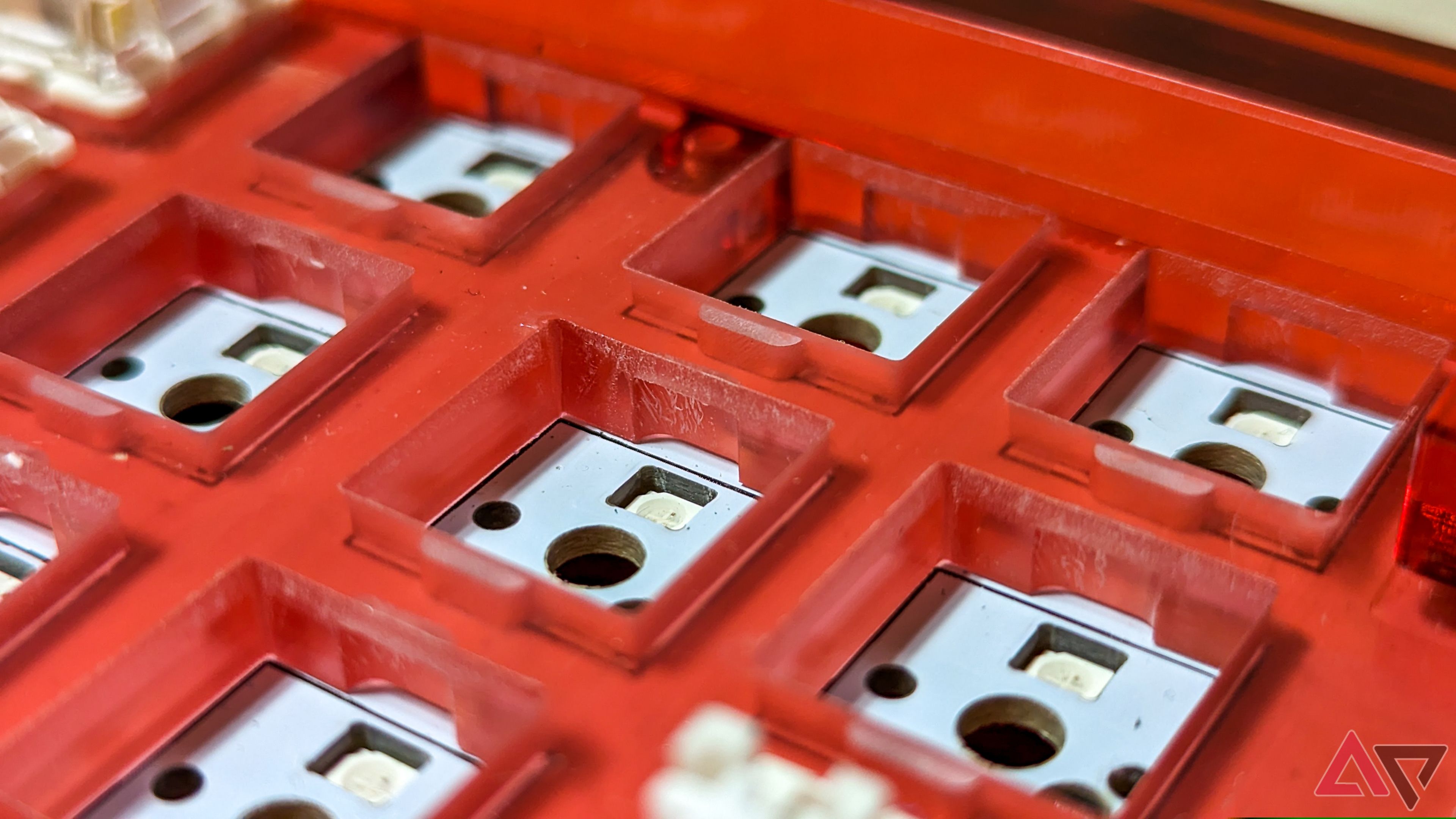 Key switch cutouts in a red acrylic keyboard with a white PCB visible underneath