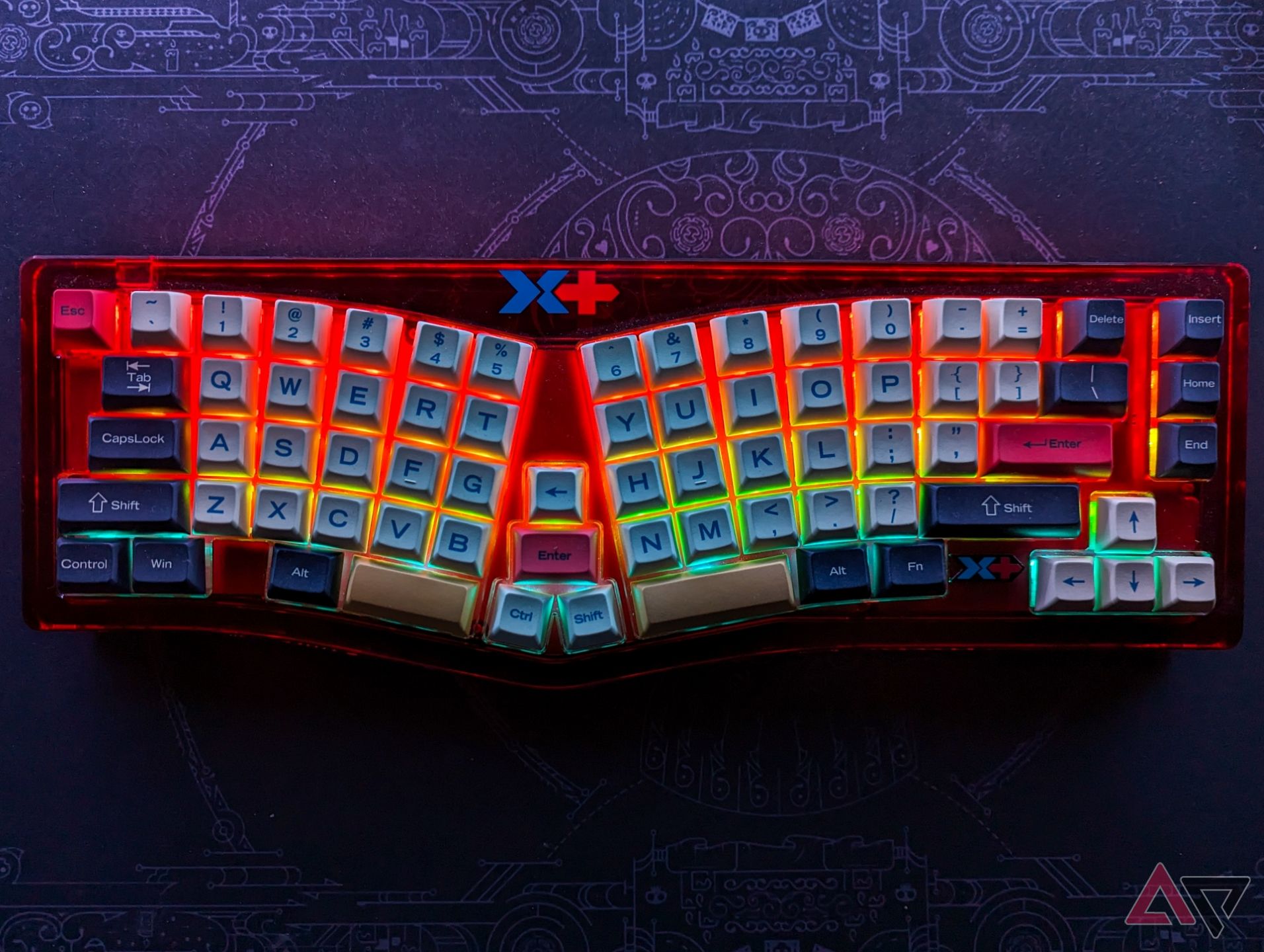 A red Alice layout mechanical keyboard with RGB backlighting on a dimly lit black deskmat