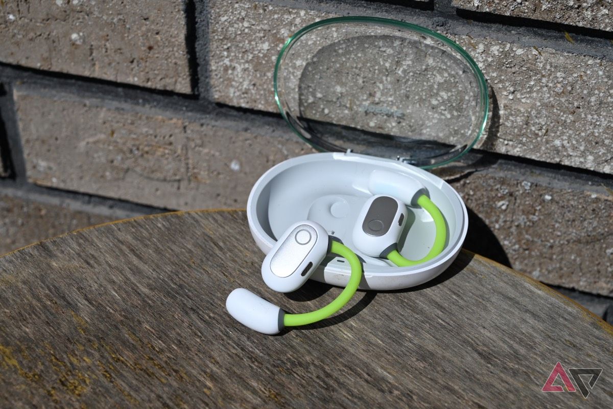 Side shot of white-and-neon-green Baseus Eli Sport 1 Open-Ear TWS earbuds on brick background with one bud in charging case.